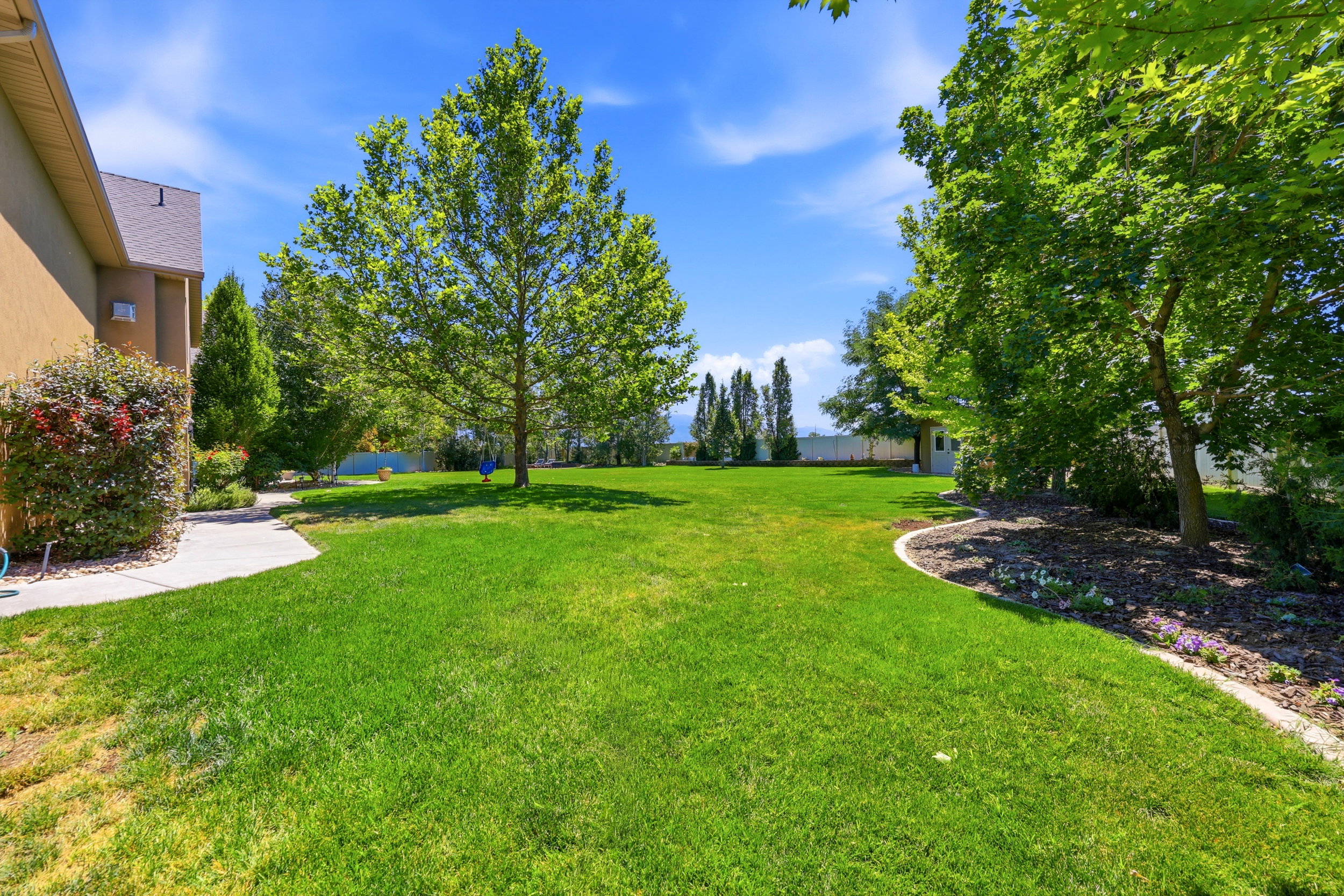 Expansive lawn area featuring mature trees and a curved concrete pathway