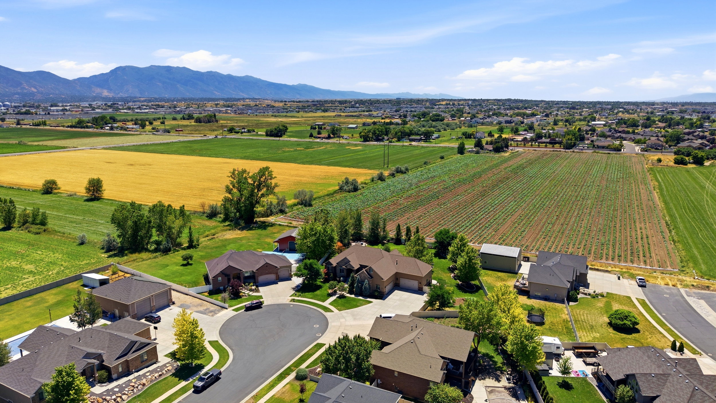 Aerial perspective showcasing a residential development bordered by agricultural fields and distant mountains