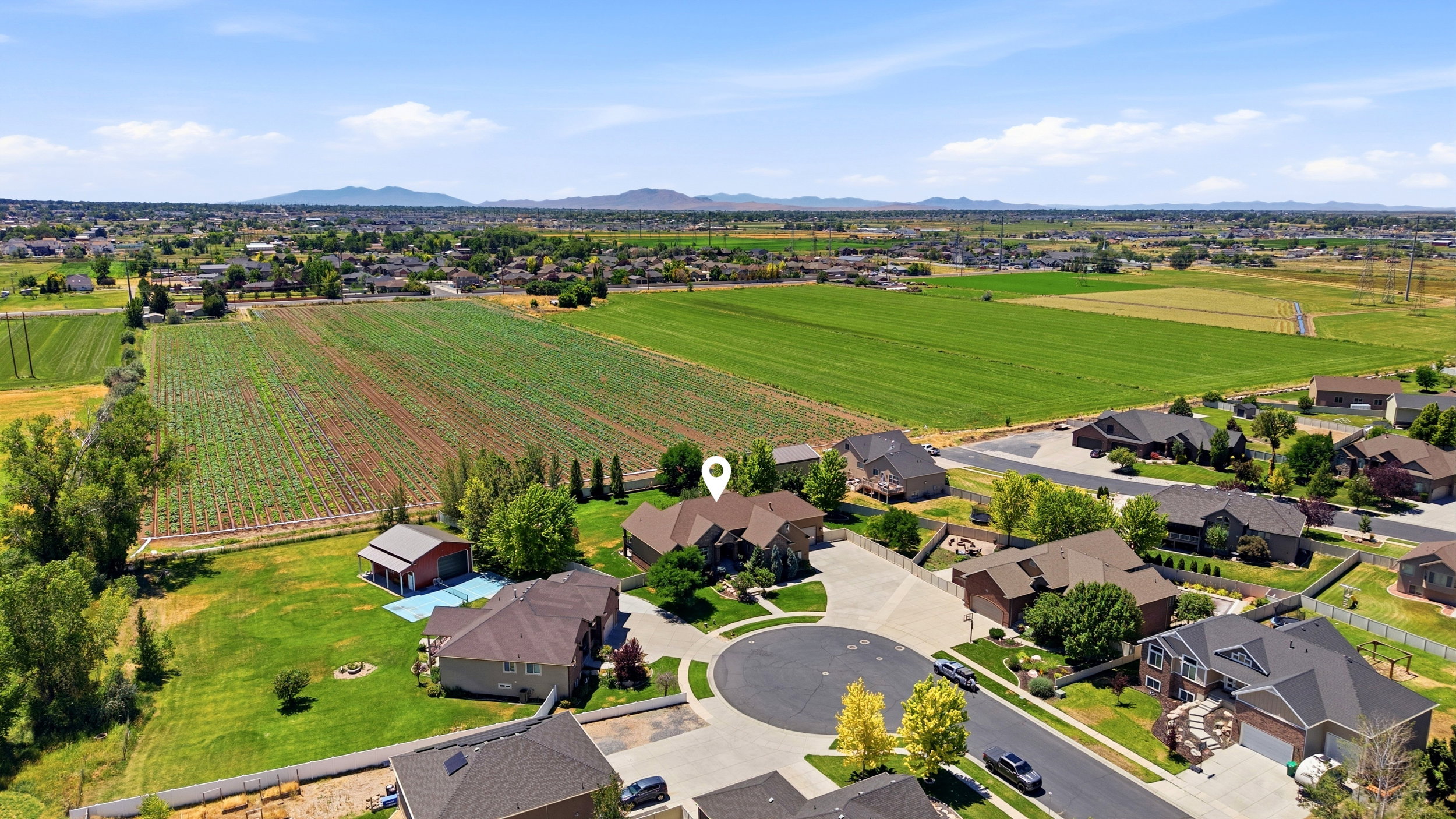 Aerial perspective showcasing a residential cul-de-sac with surrounding agricultural fields and distant mountains