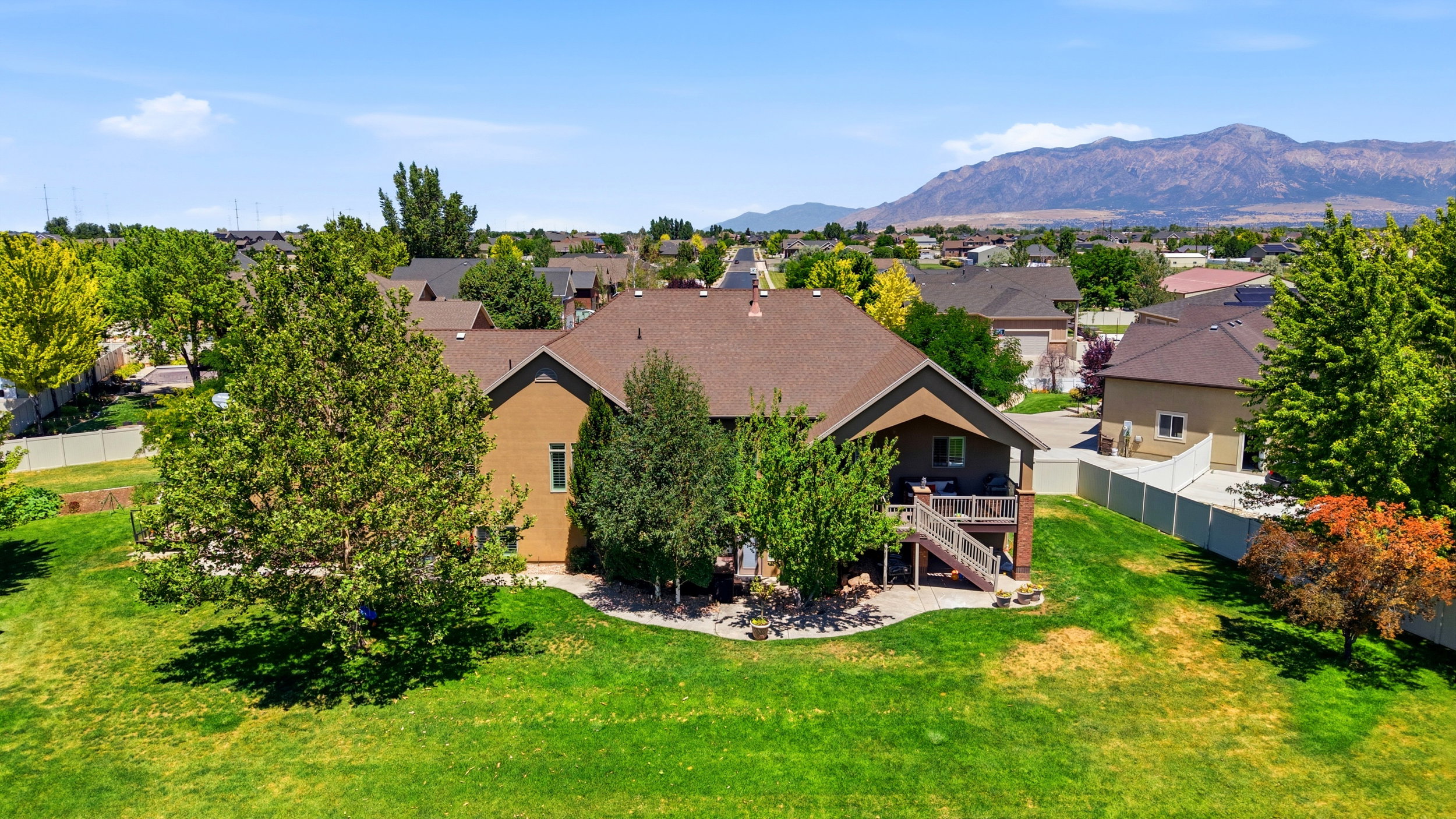 Expansive backyard featuring a manicured lawn, mature trees, and a multi-level wooden deck with stairs