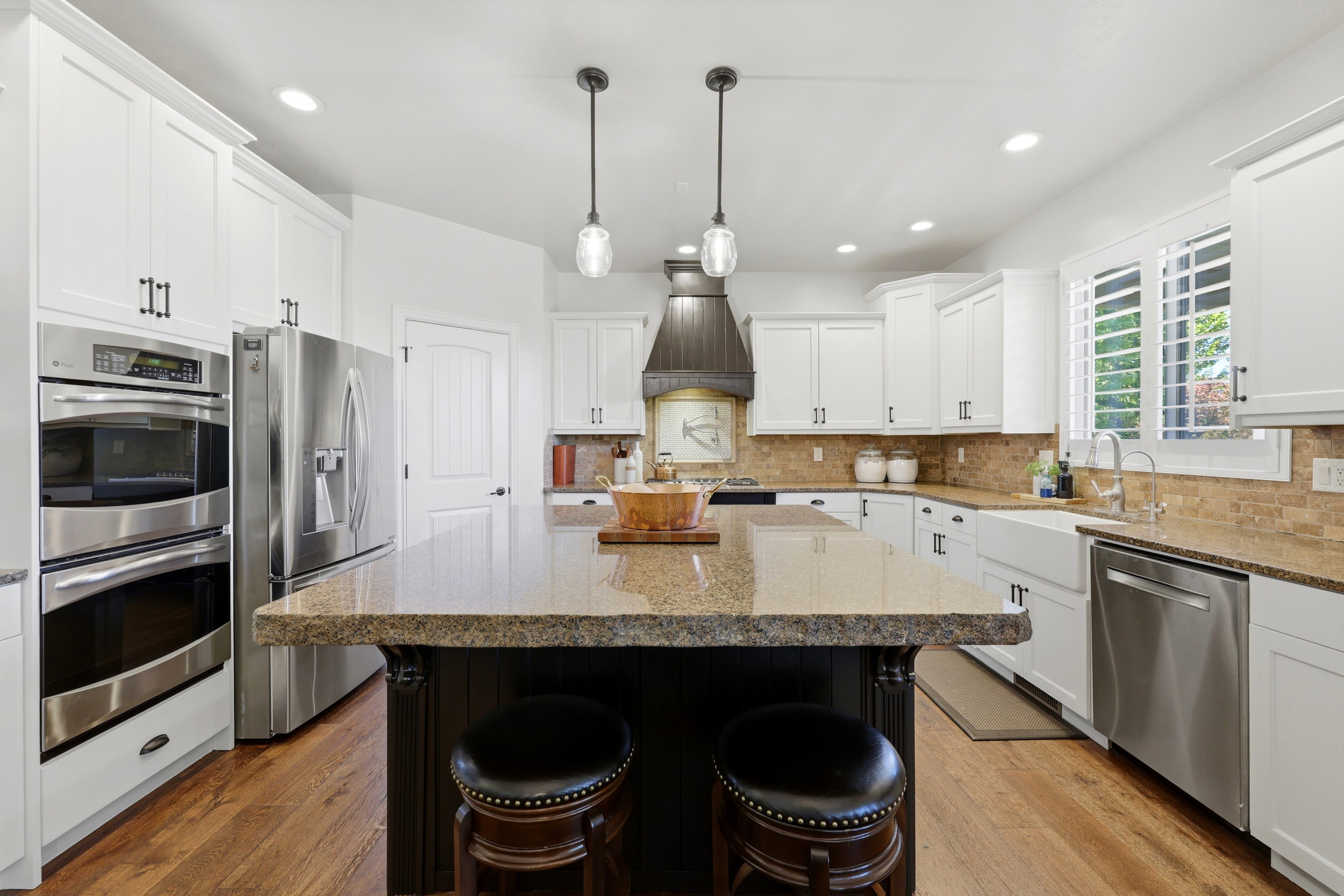 Kitchen featuring a central island with a granite countertop, white shaker-style cabinetry, stainless steel appliances, and wood-finish flooring