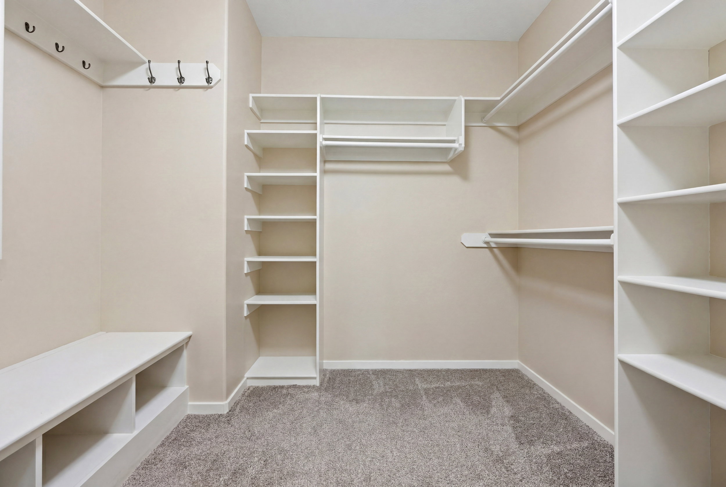 Integrated closet system featuring multiple hanging rods, built-in shelving, a storage bench, and wall-mounted hooks