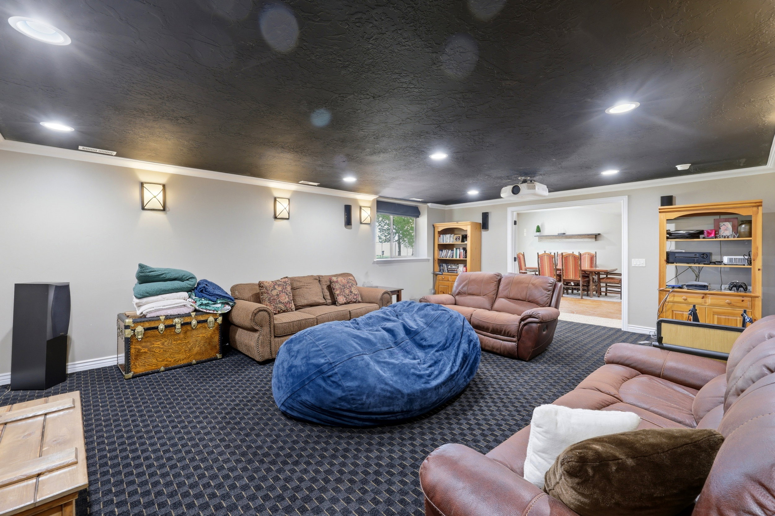 Spacious recreation area featuring recessed lighting, wall sconces, dark patterned carpeting, a dark ceiling, and an open entryway to an adjacent room