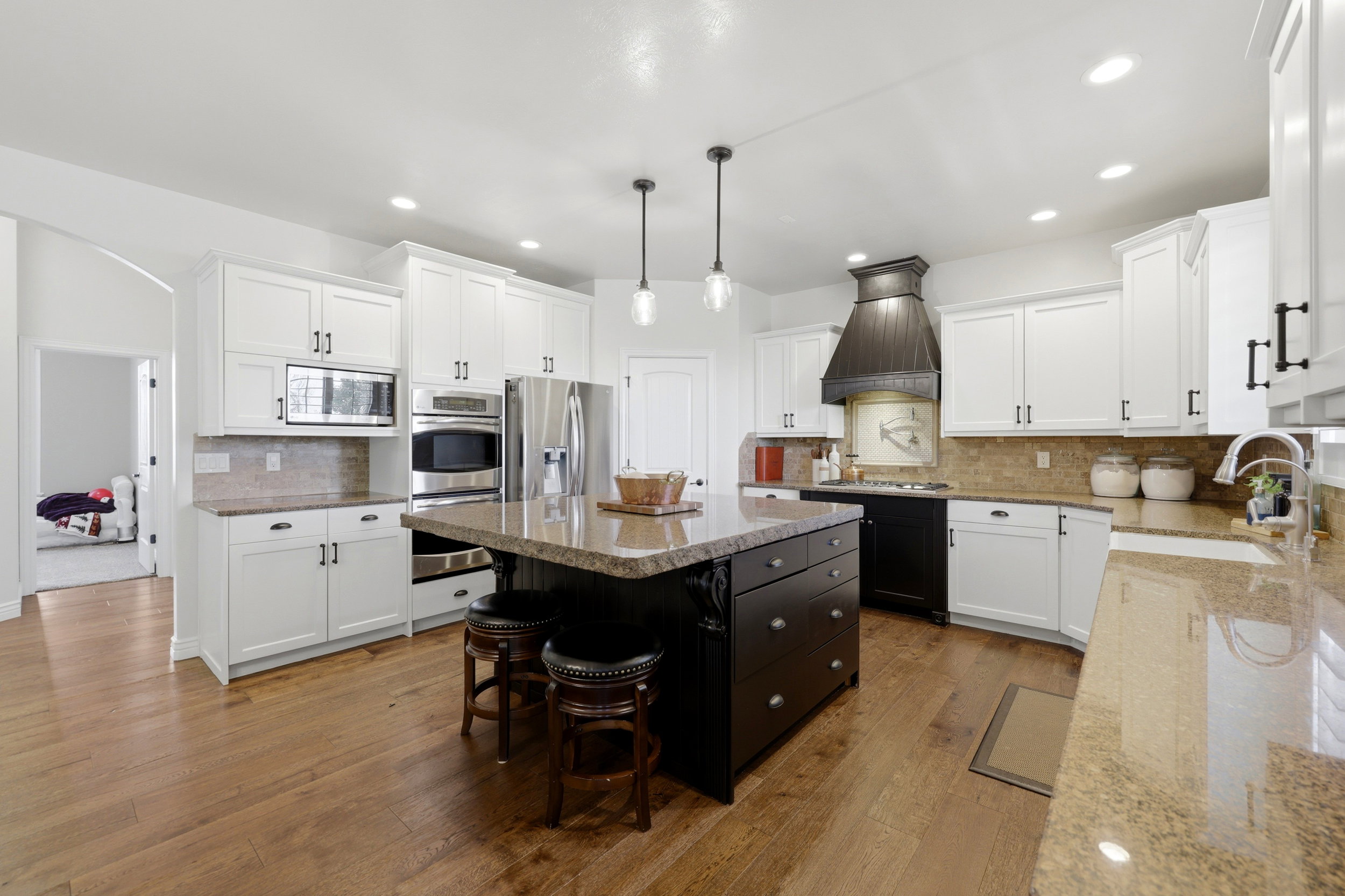 Kitchen featuring a large island with seating, stainless steel appliances, wood-finish flooring, white cabinetry, and recessed lighting