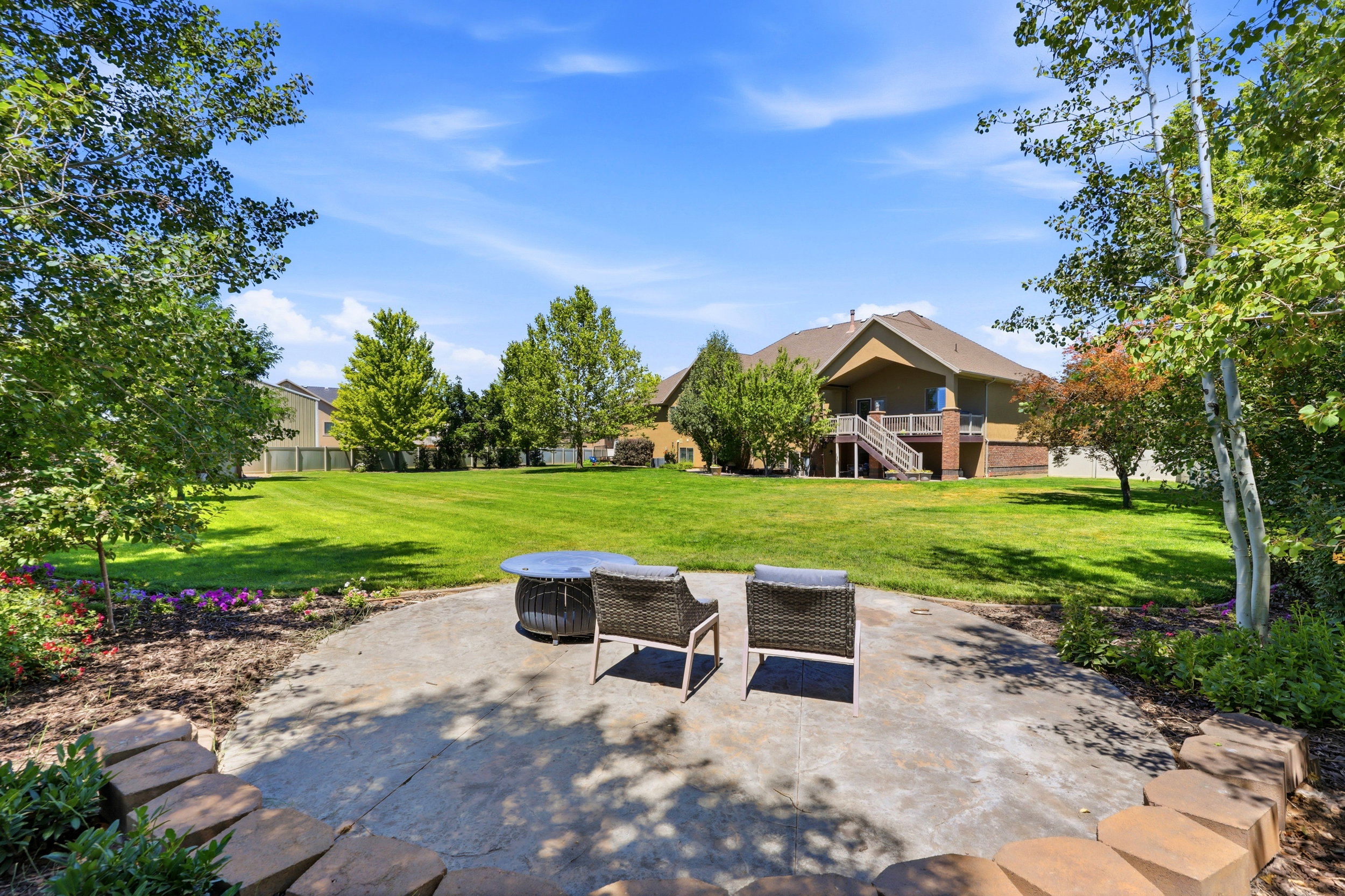 Expansive backyard featuring a large concrete patio, stone retaining wall, and mature trees