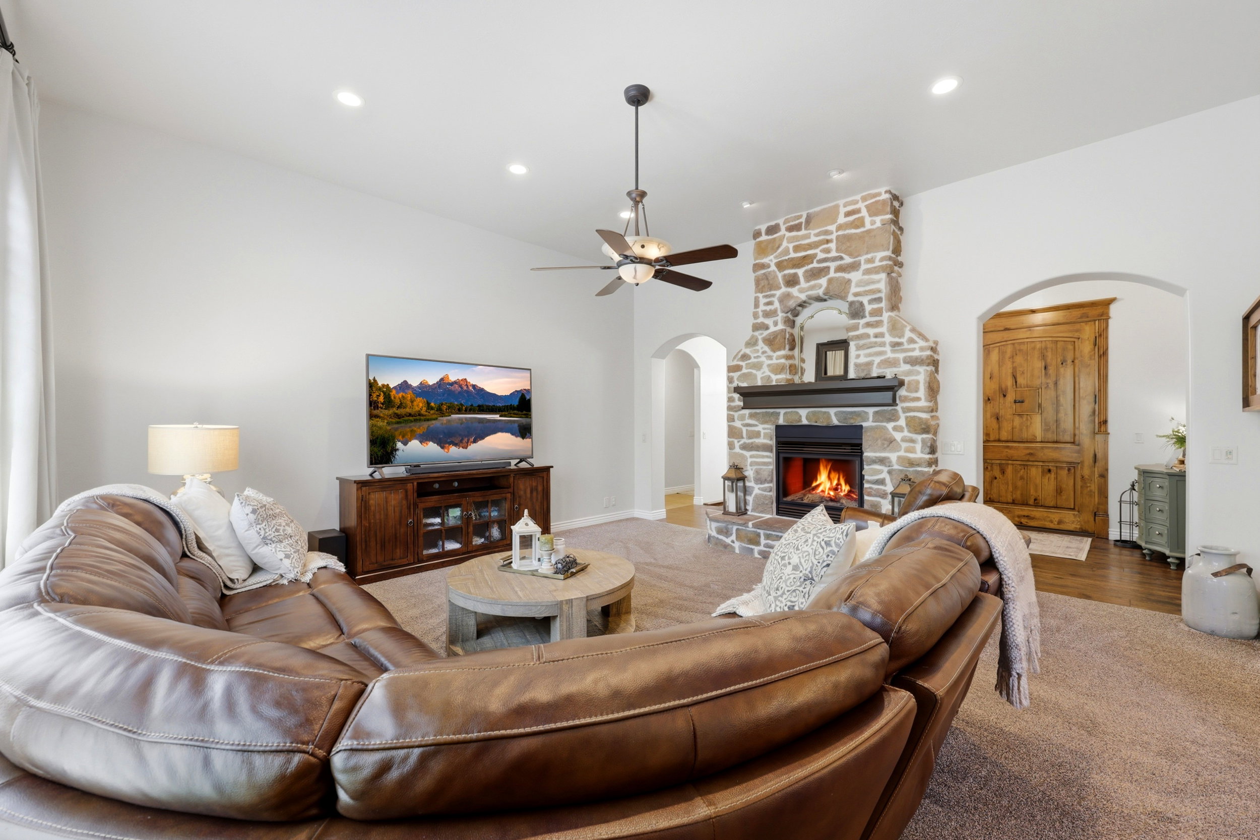 Spacious living area featuring a stone-clad fireplace with a dark wood mantel, vaulted ceilings, recessed lighting, and a ceiling fan