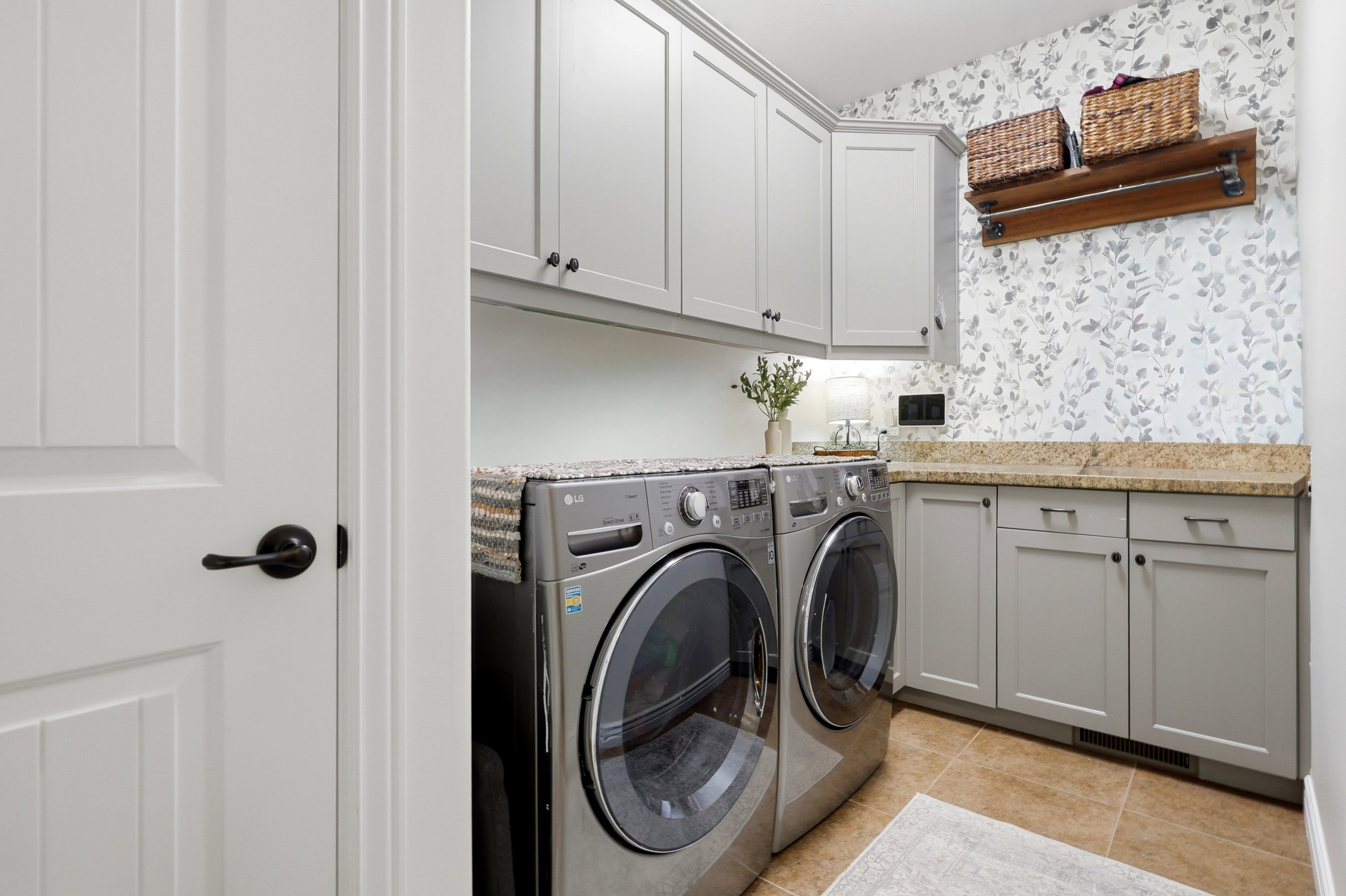Dedicated utility space featuring light gray cabinetry, a stone-finish countertop, and decorative wall covering