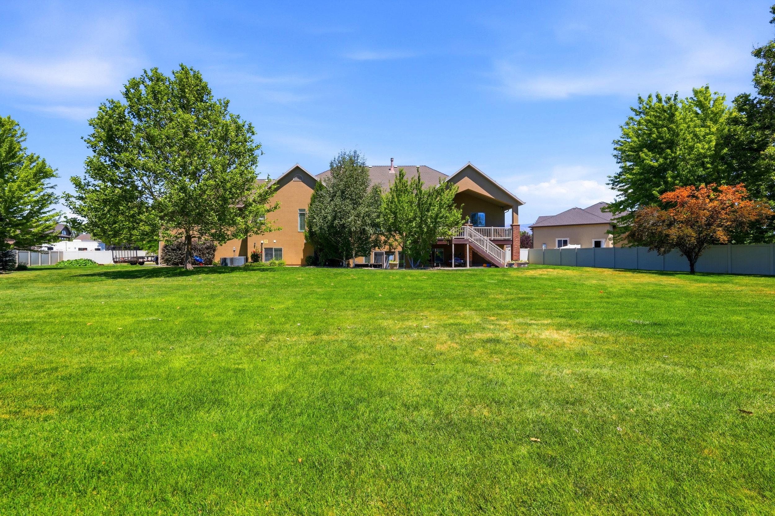Expansive green lawn with mature trees and a privacy fence bordering the property