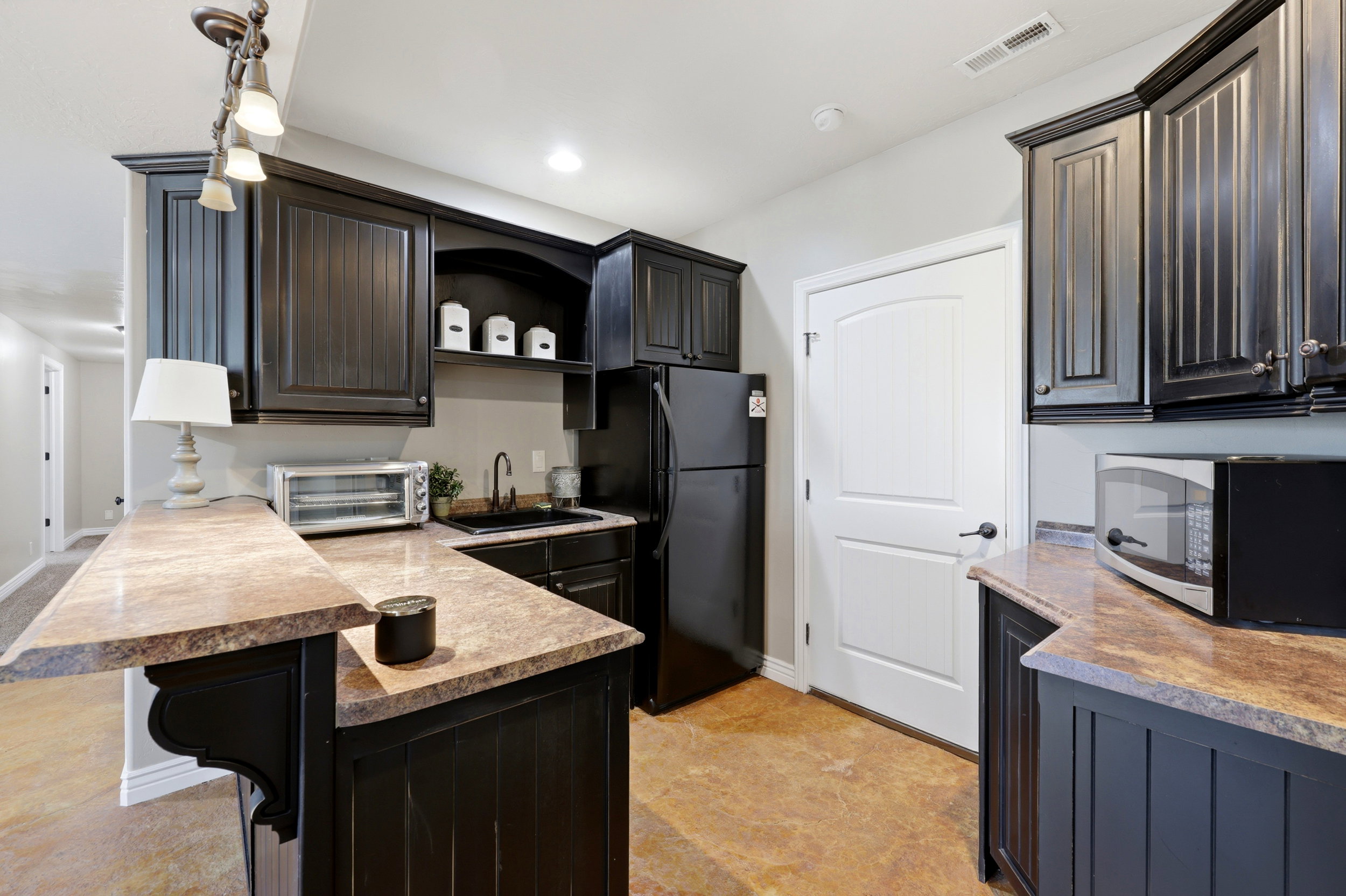 Compact kitchenette featuring dark wood cabinetry, a sink with a black faucet, and stone-finish countertops