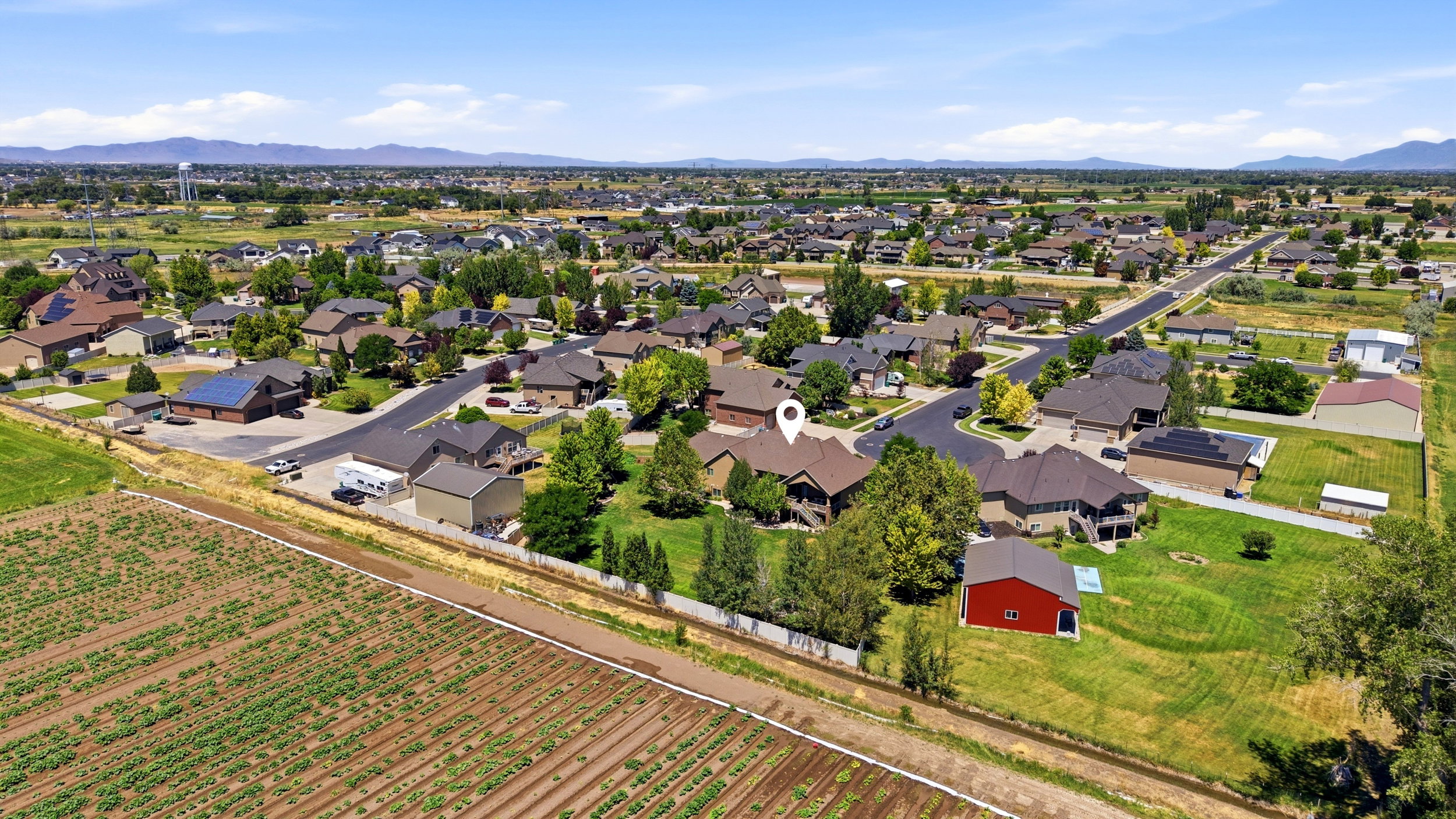 Aerial perspective showcasing a residential neighborhood with surrounding agricultural fields and distant mountains