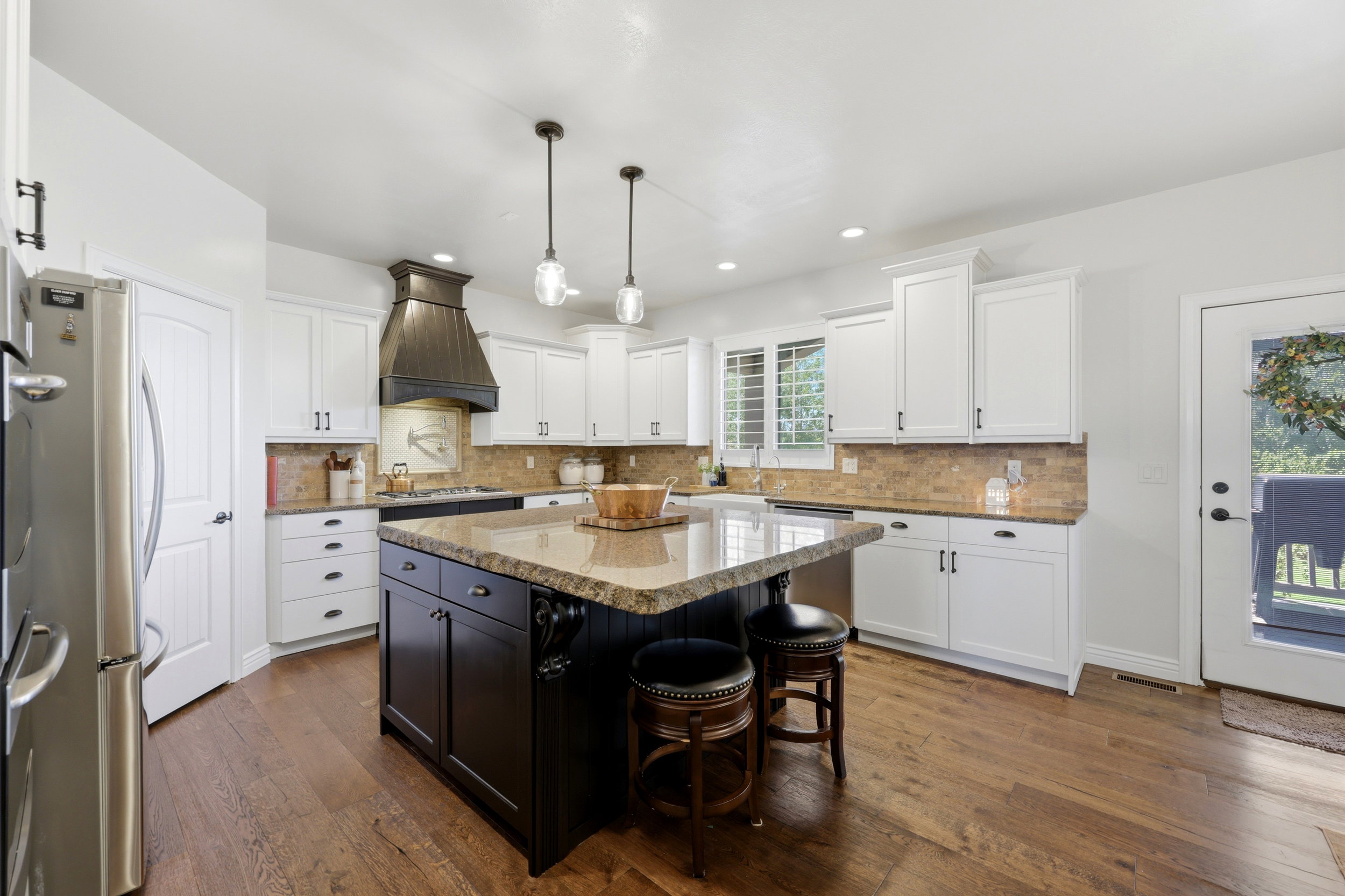 Kitchen featuring a large island with granite countertop, white cabinetry with dark hardware, a decorative range hood, stainless steel appliances, and wood-finish flooring