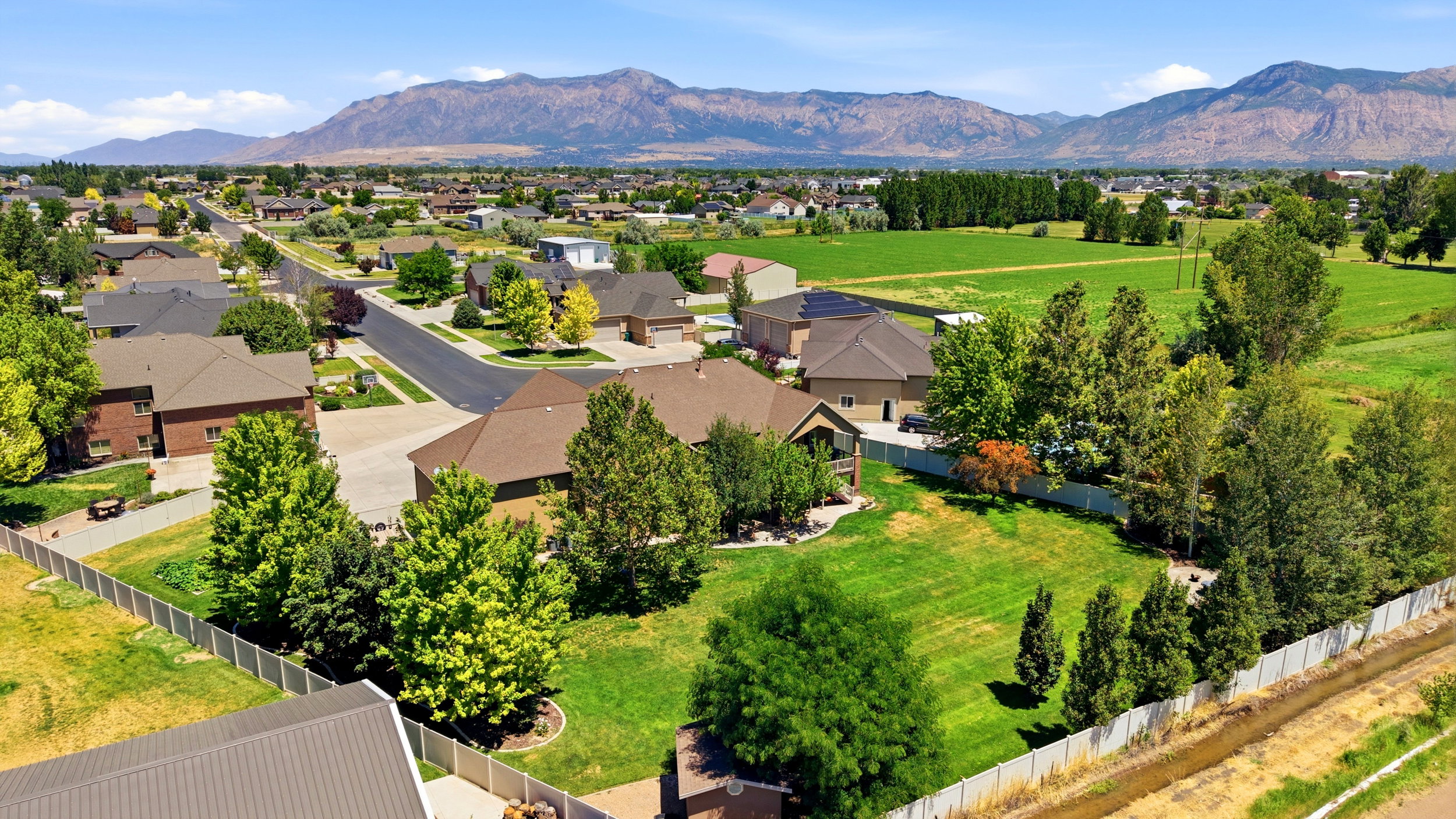 Expansive green space with mature trees, fenced perimeter, and a distant mountain range backdrop