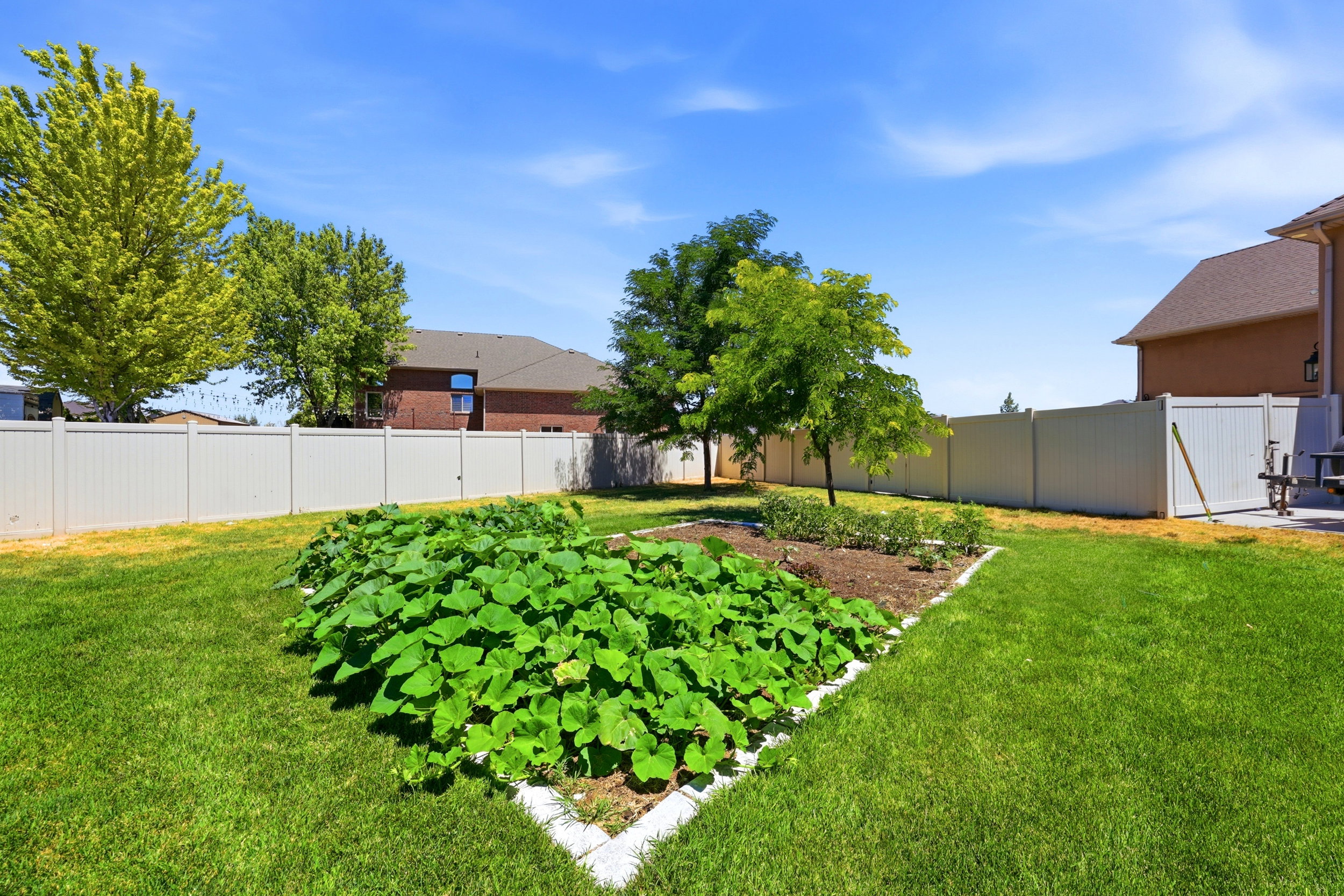 Spacious backyard featuring a large garden bed, mature trees, manicured lawn, and perimeter fencing