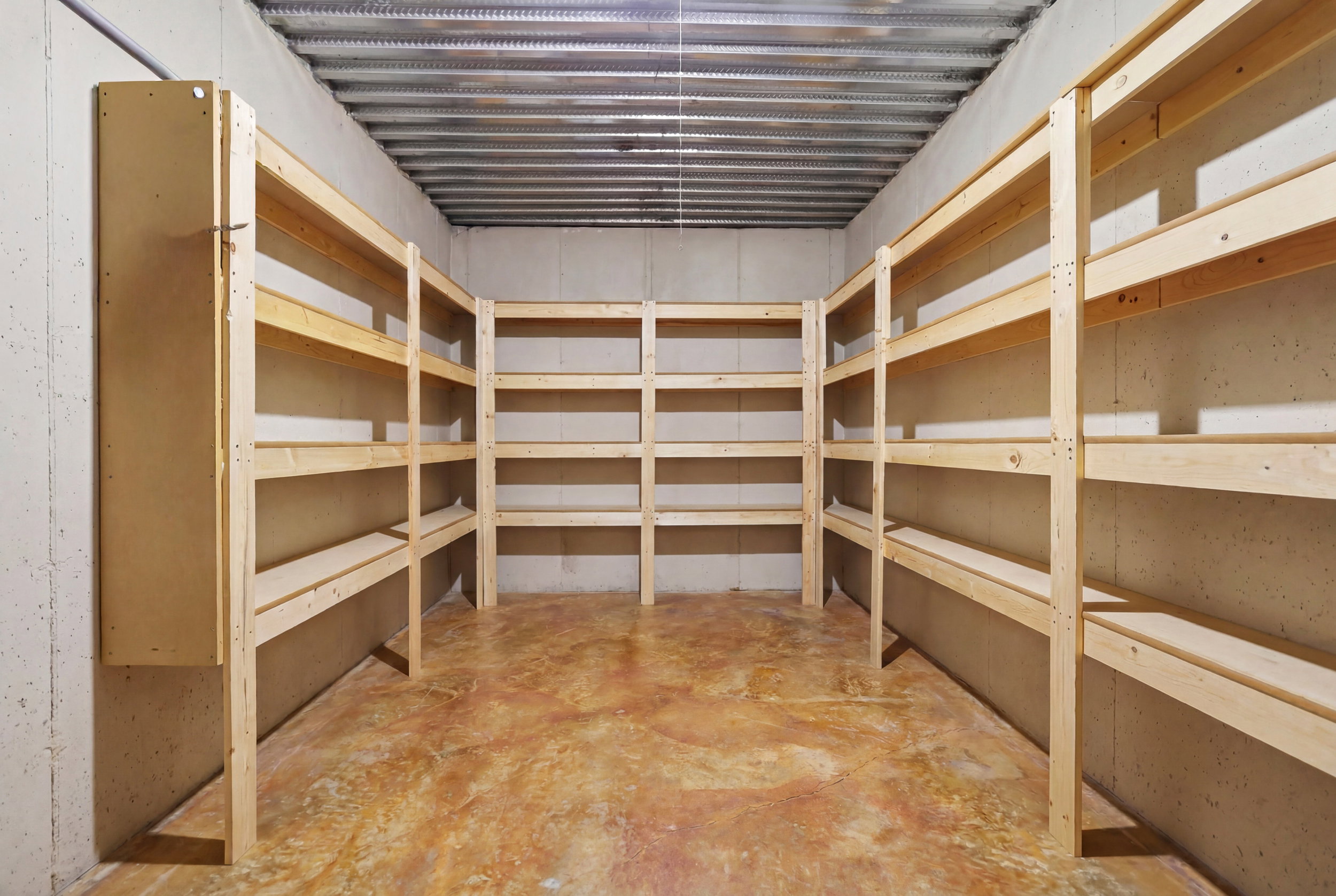 Basement storage area featuring extensive built-in wooden shelving, concrete walls, and a corrugated metal ceiling