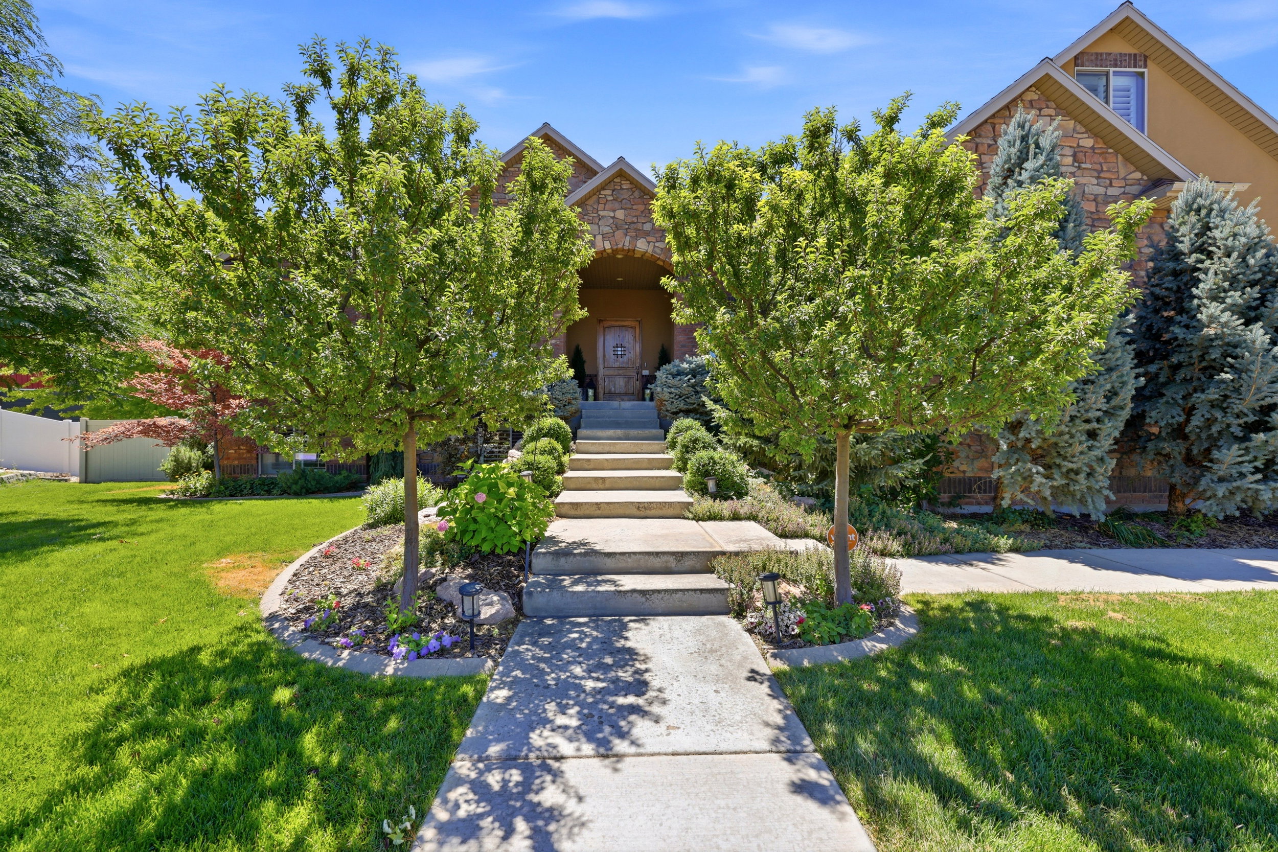 Stone facade residence featuring a grand arched entryway, concrete walkway, and tiered stone steps