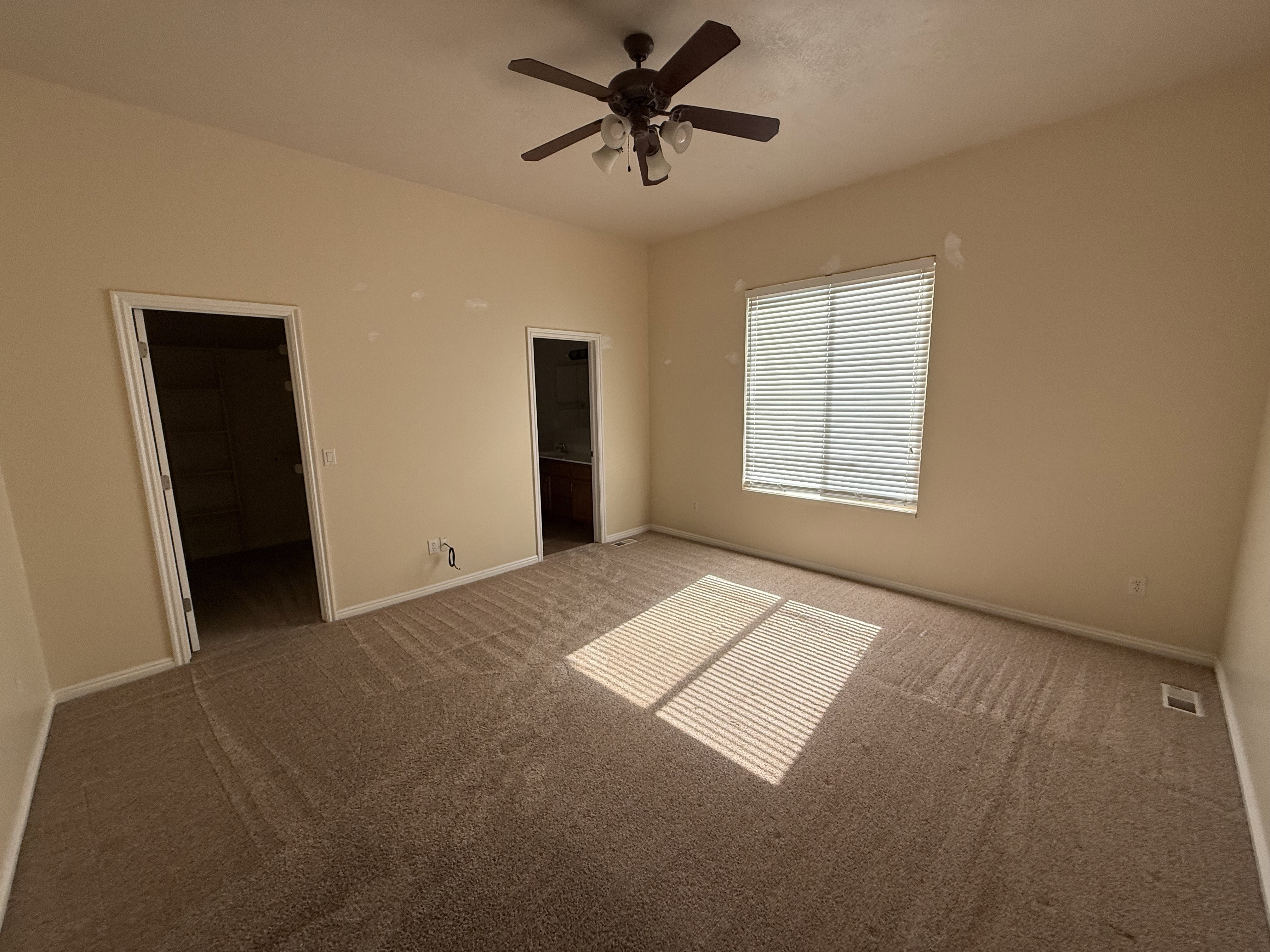 Carpeted room featuring a ceiling fan with light fixture, a window with horizontal blinds, and two doorways