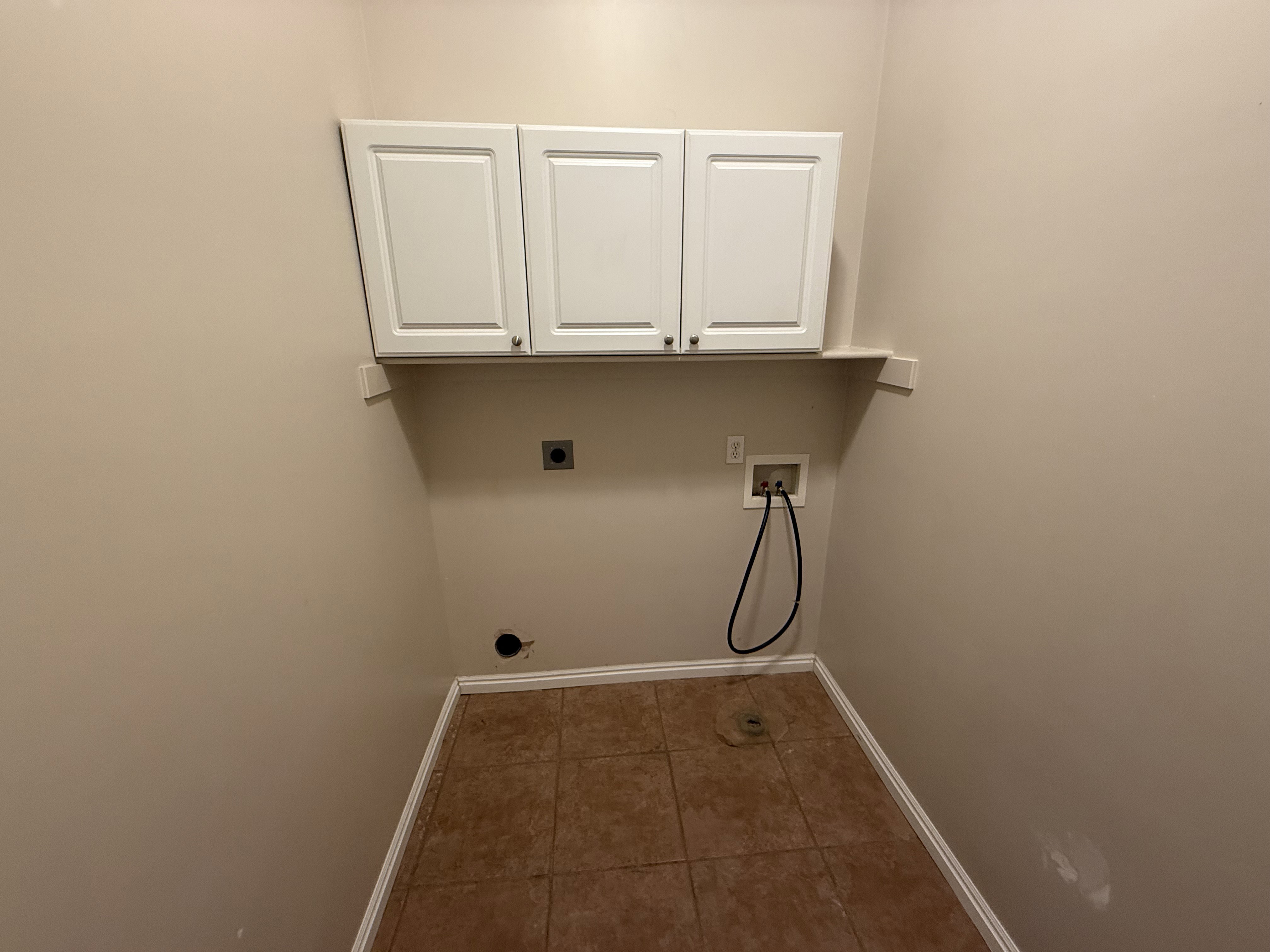 Laundry area featuring upper white cabinetry, a built-in shelf, tile flooring, and neutral wall paint