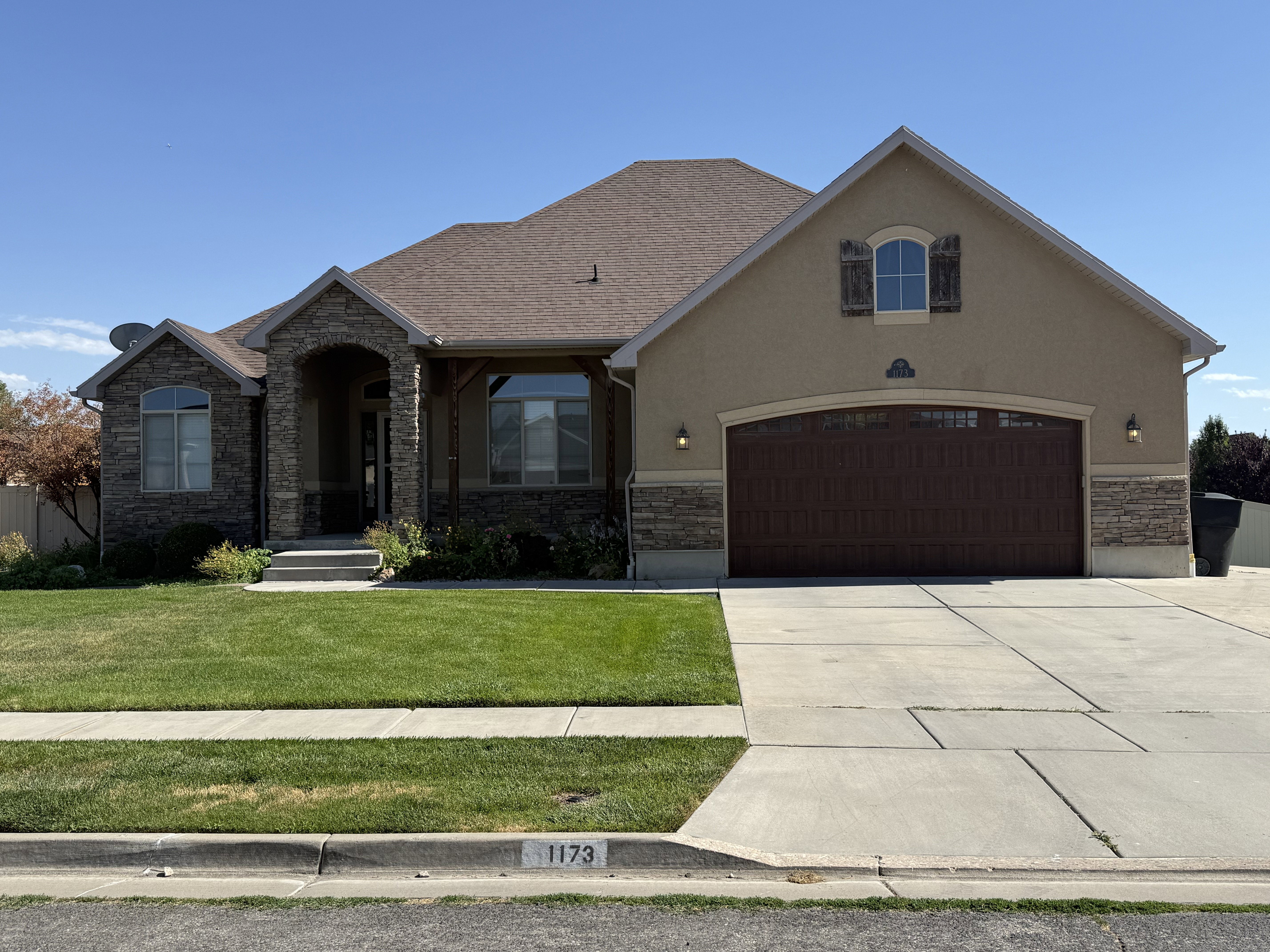 Ranch-style residence featuring a stucco and stone facade, arched entryway, and an attached two-car garage with a wood-finish door