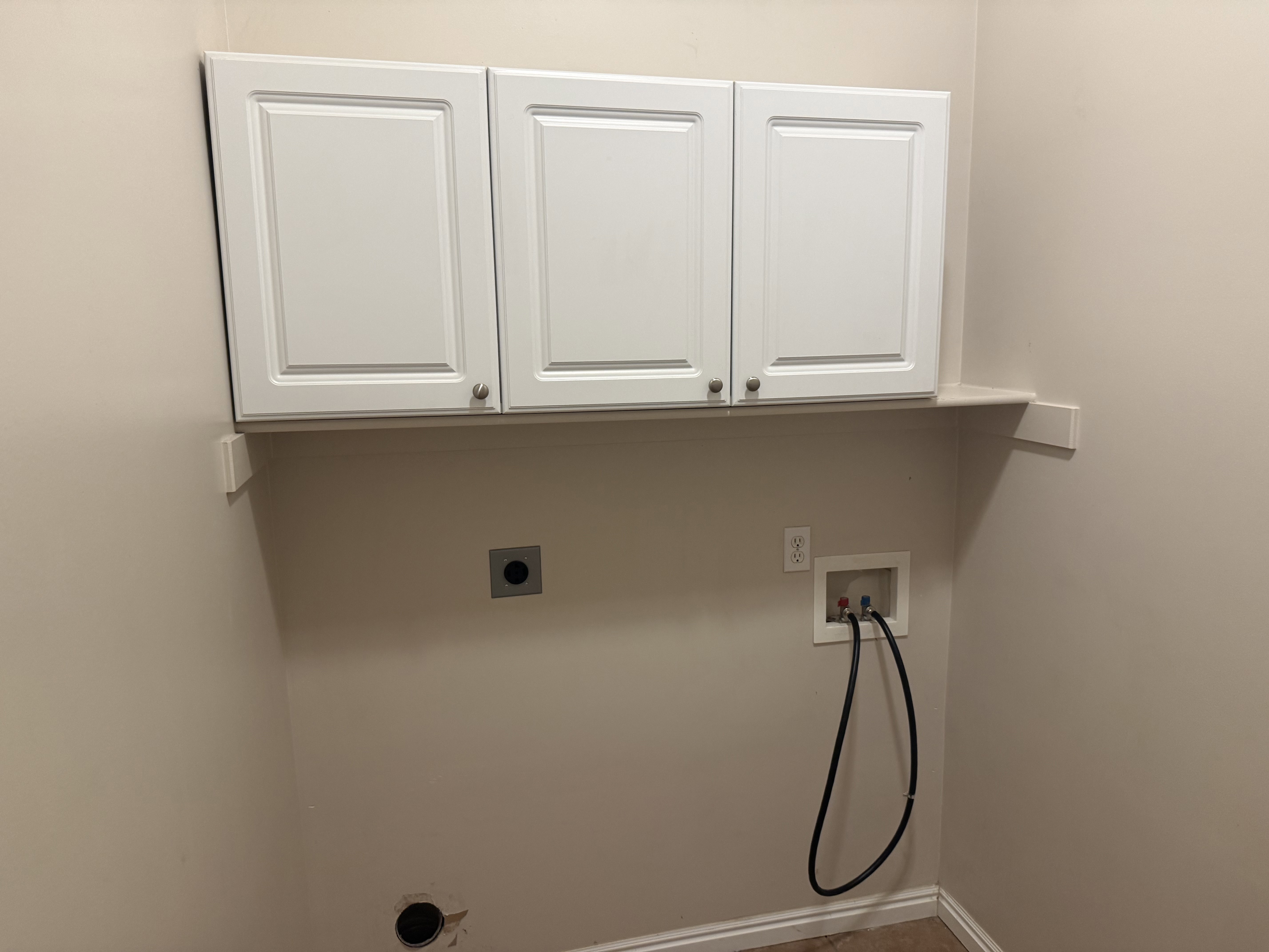 Laundry area featuring three white shaker-style cabinets with brushed nickel hardware, a utility shelf, and laundry hookups