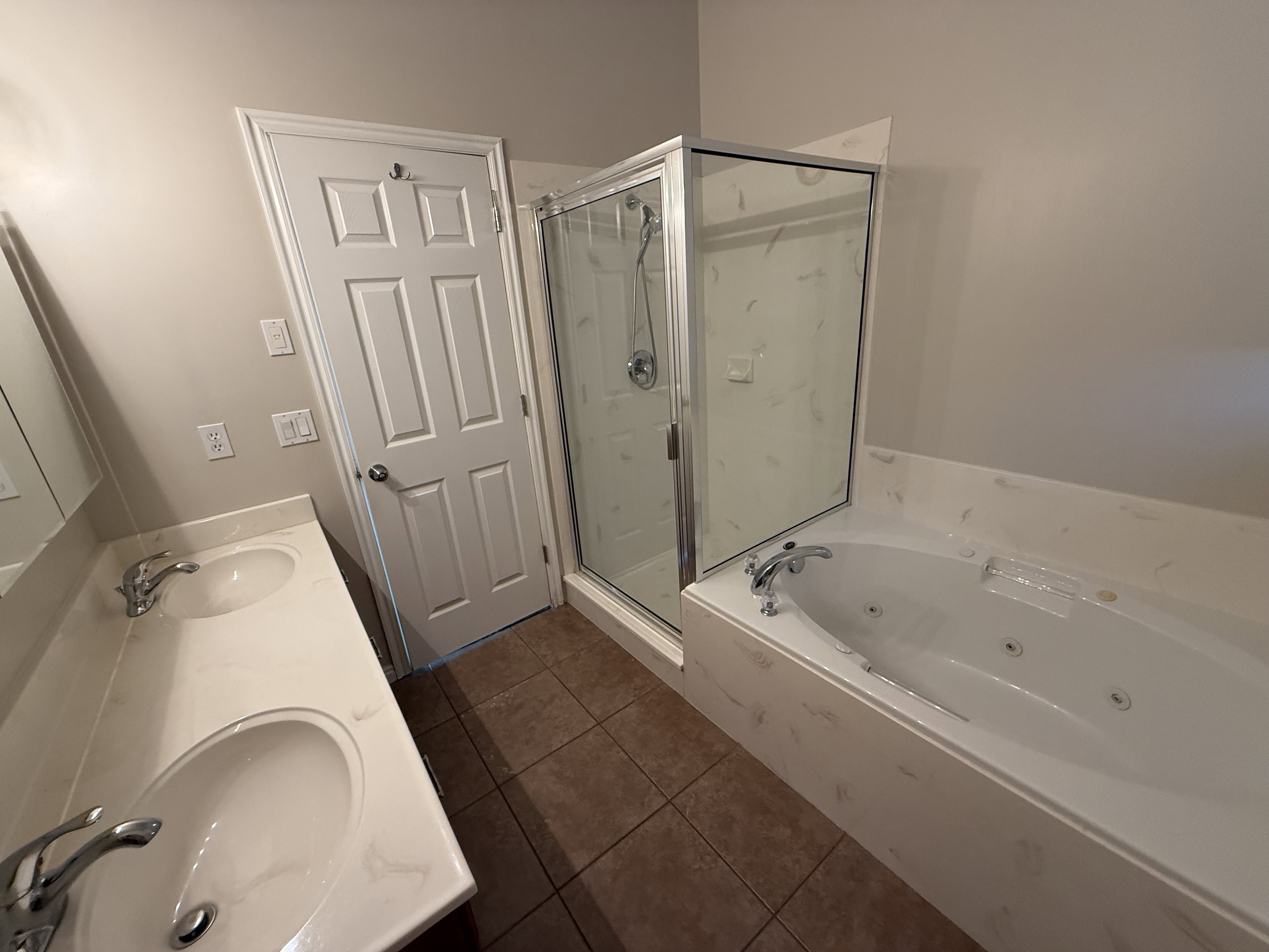 Bathroom featuring a dual vanity with undermount sinks, a built-in jetted tub, a glass-enclosed shower, and brown tile flooring