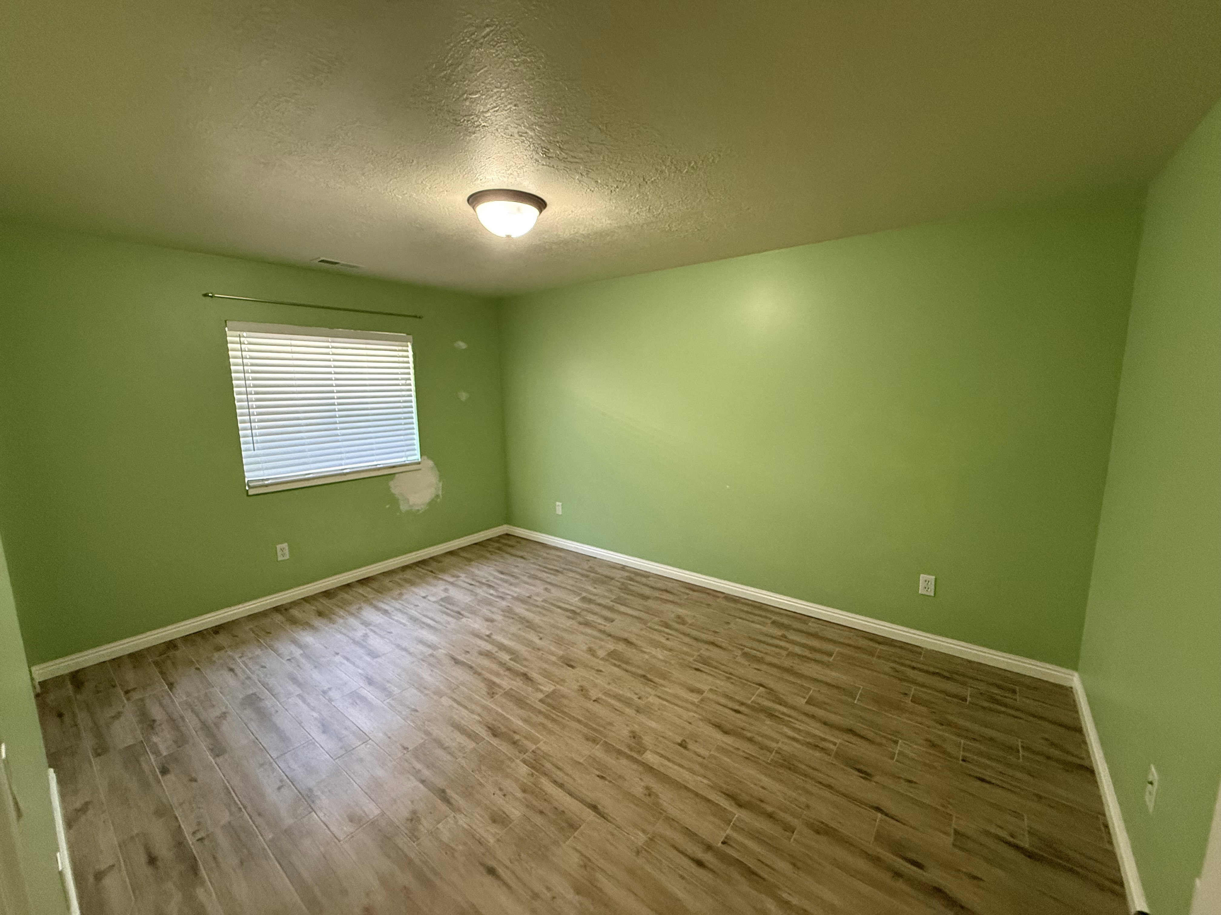 Spacious room featuring wood-finish flooring, a window with blinds, and a ceiling-mounted light fixture