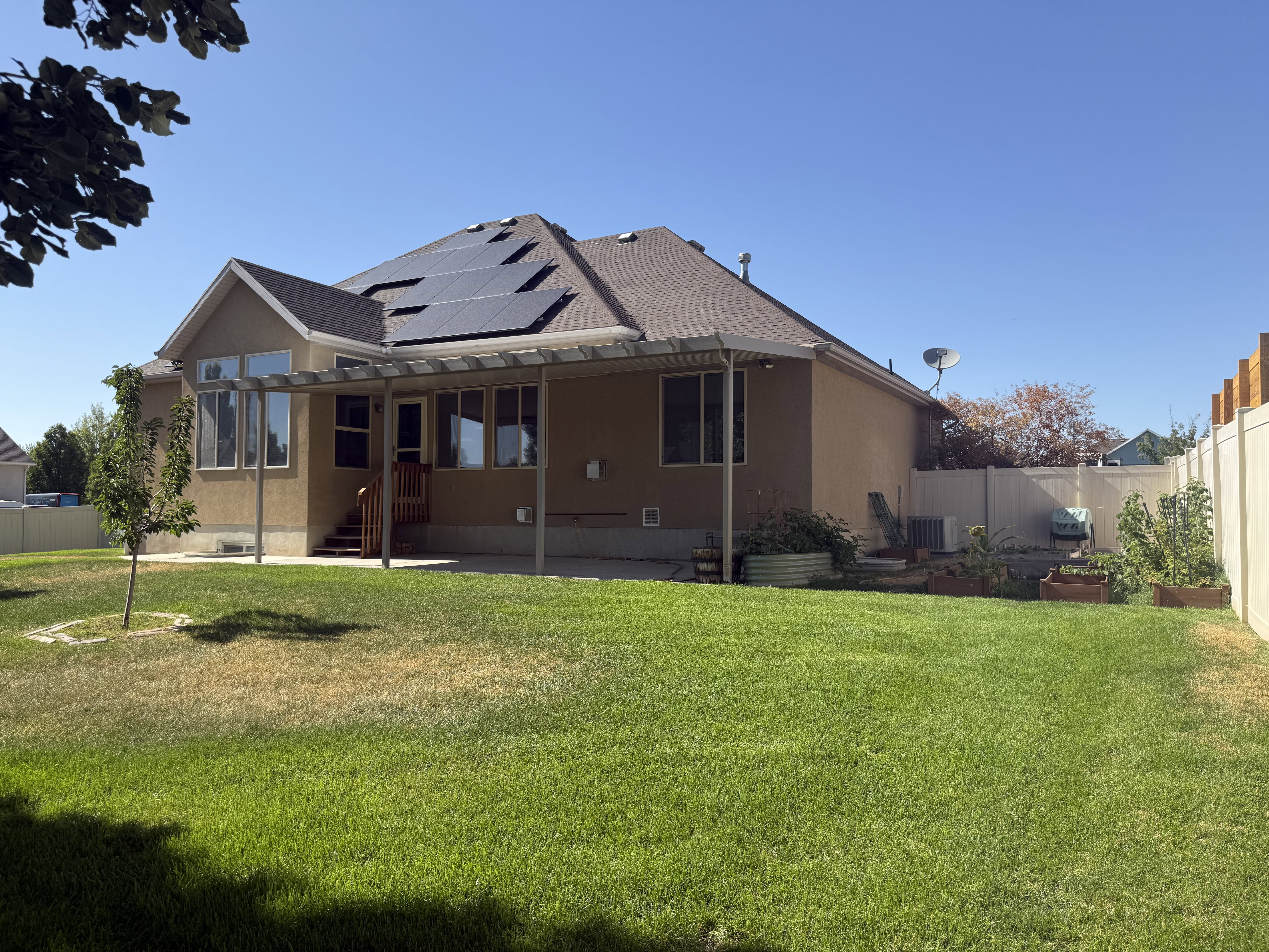 Spacious backyard featuring a large green lawn, a covered patio structure, and multiple raised garden beds