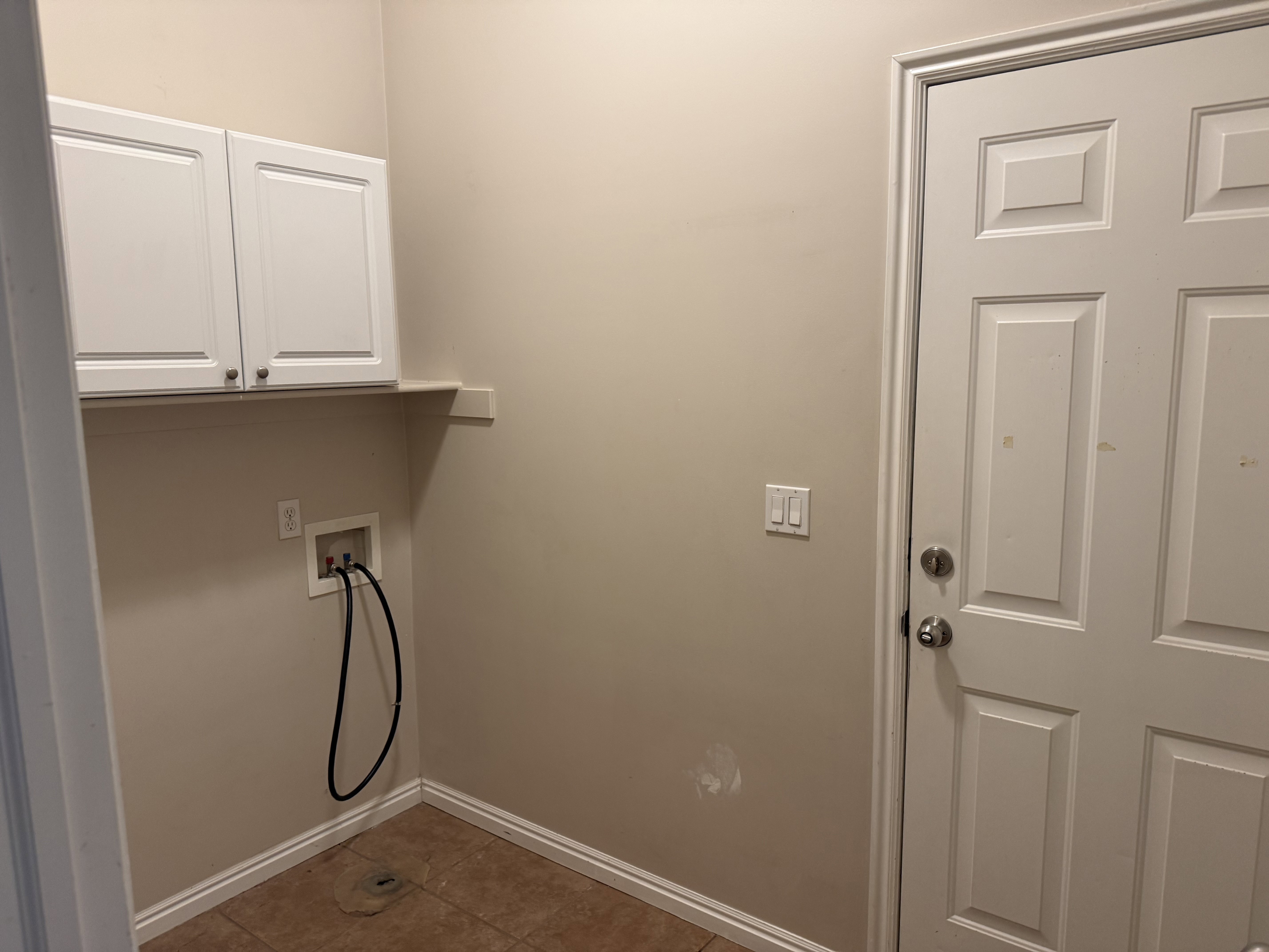 Laundry area featuring two white upper cabinets, a built-in shelf, and a tiled floor
