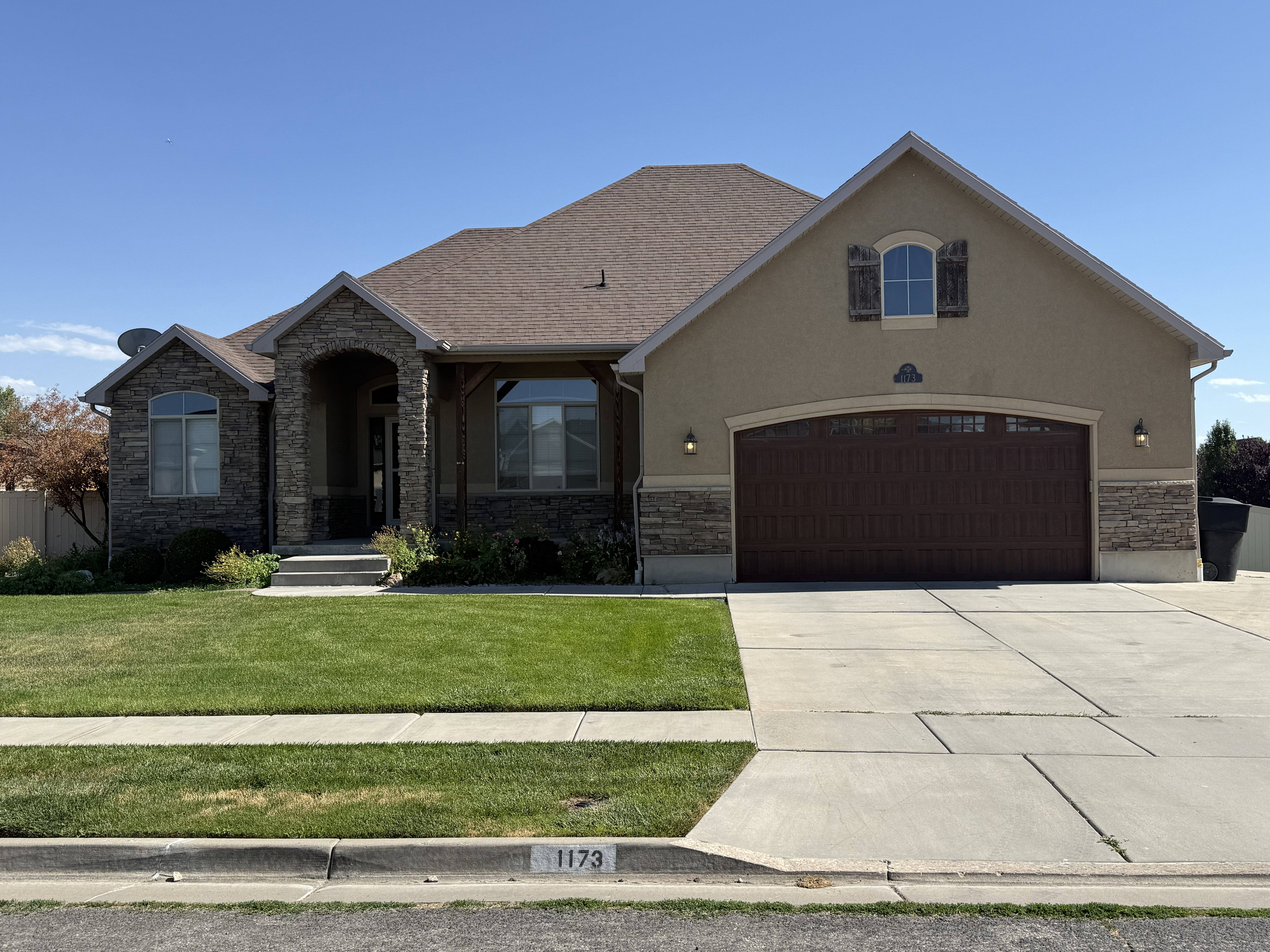 Stucco and stone facade with arched entry, complementing stone accents, and a prominent dark wood-finish garage door