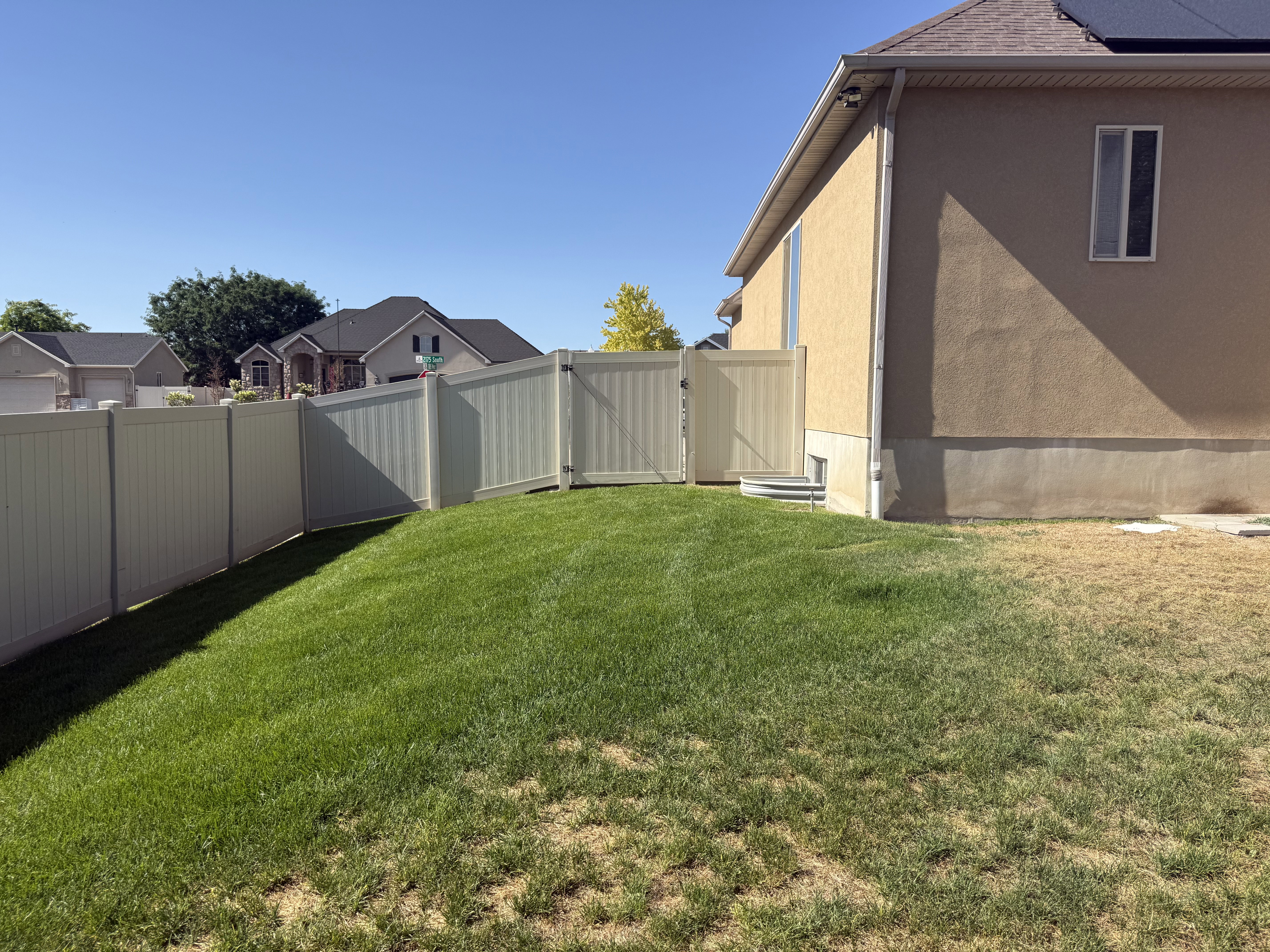 Fenced backyard featuring a manicured lawn, vinyl privacy fencing with gate, and stucco exterior