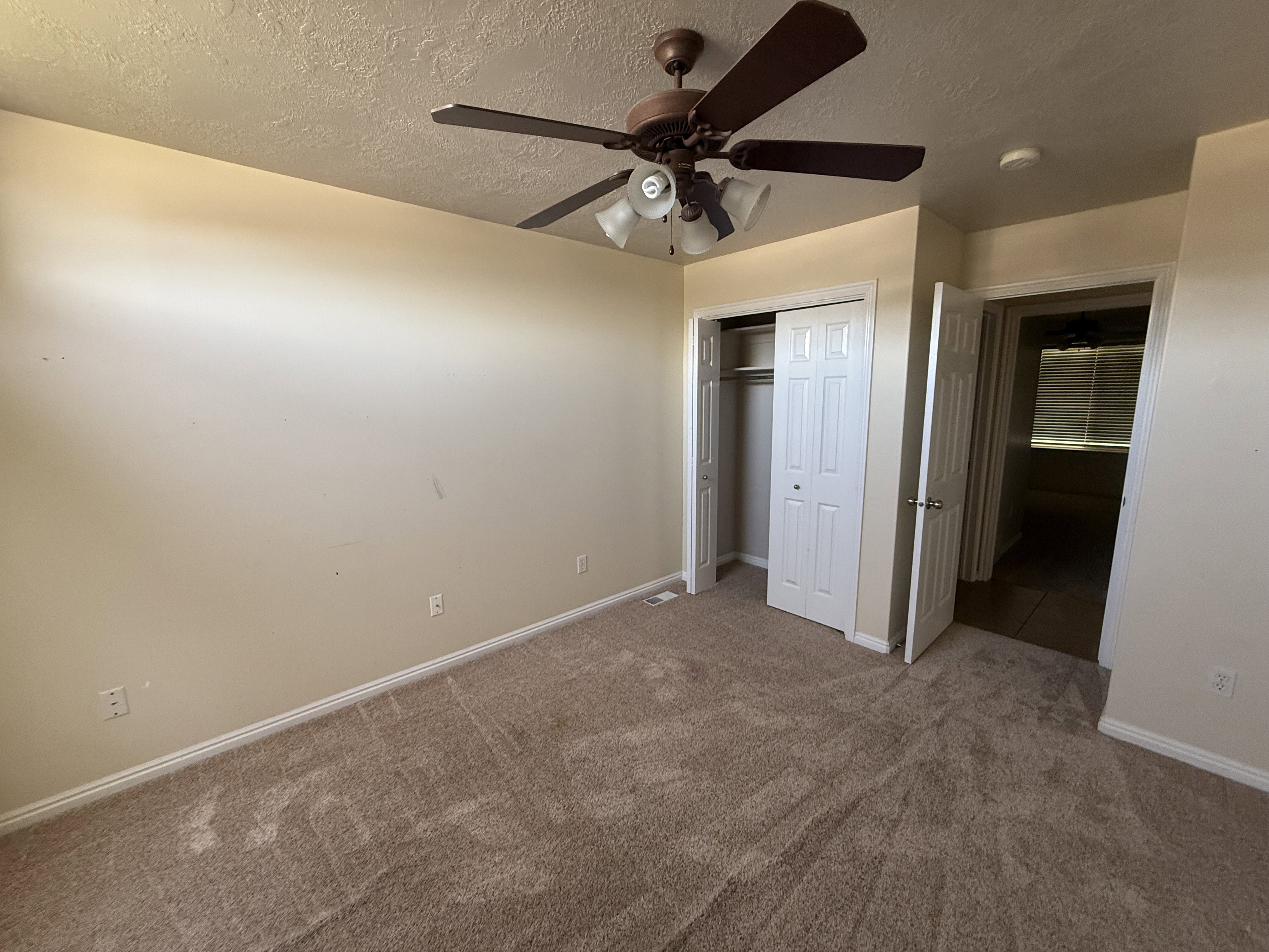 Carpeted interior space featuring a ceiling fan with integrated lighting, a bi-fold door closet, and a doorway opening to another room