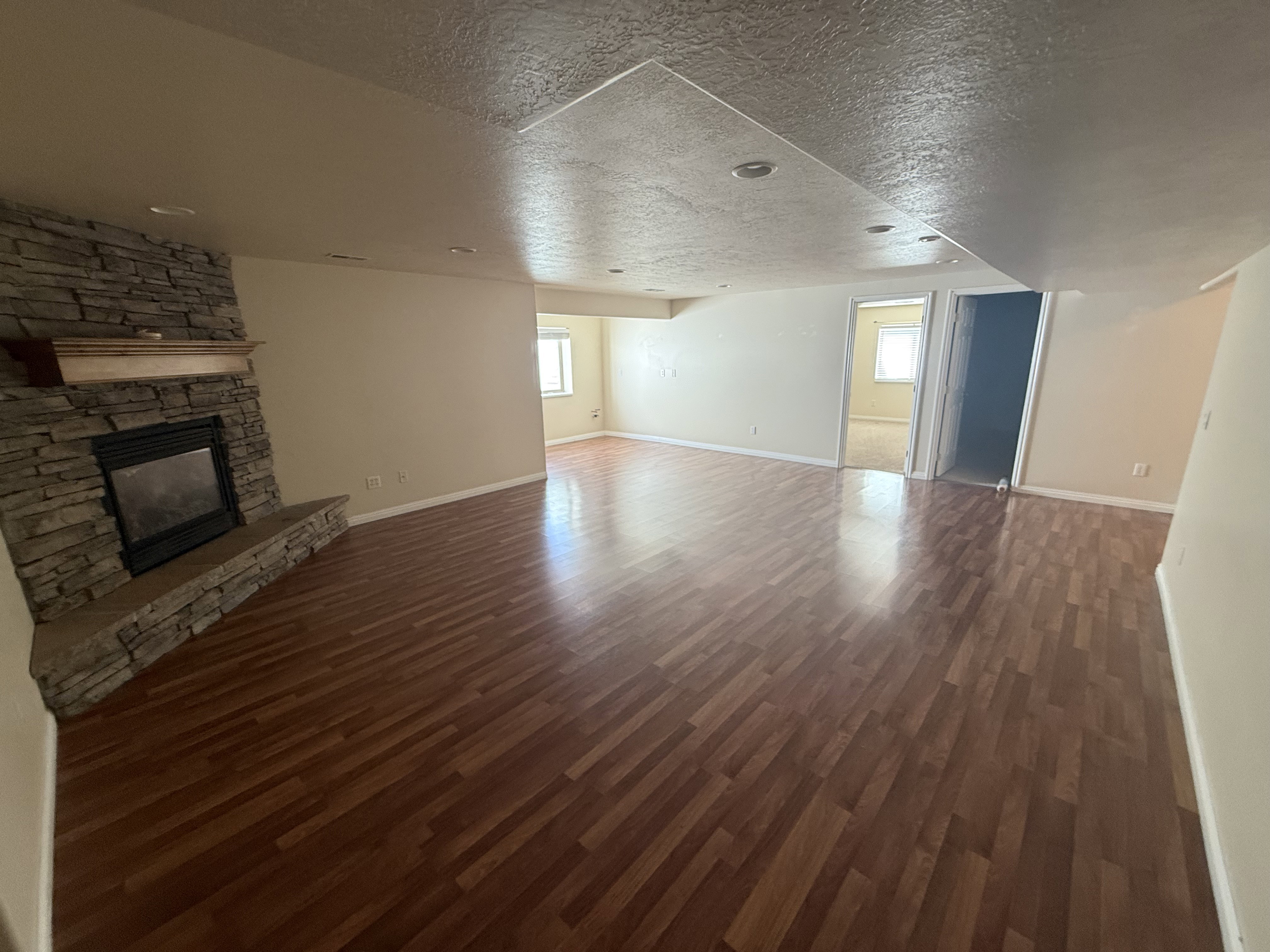 Spacious living area featuring wood-finish flooring, a stacked stone fireplace with a substantial hearth and wood mantle, recessed lighting, and neutral wall paint