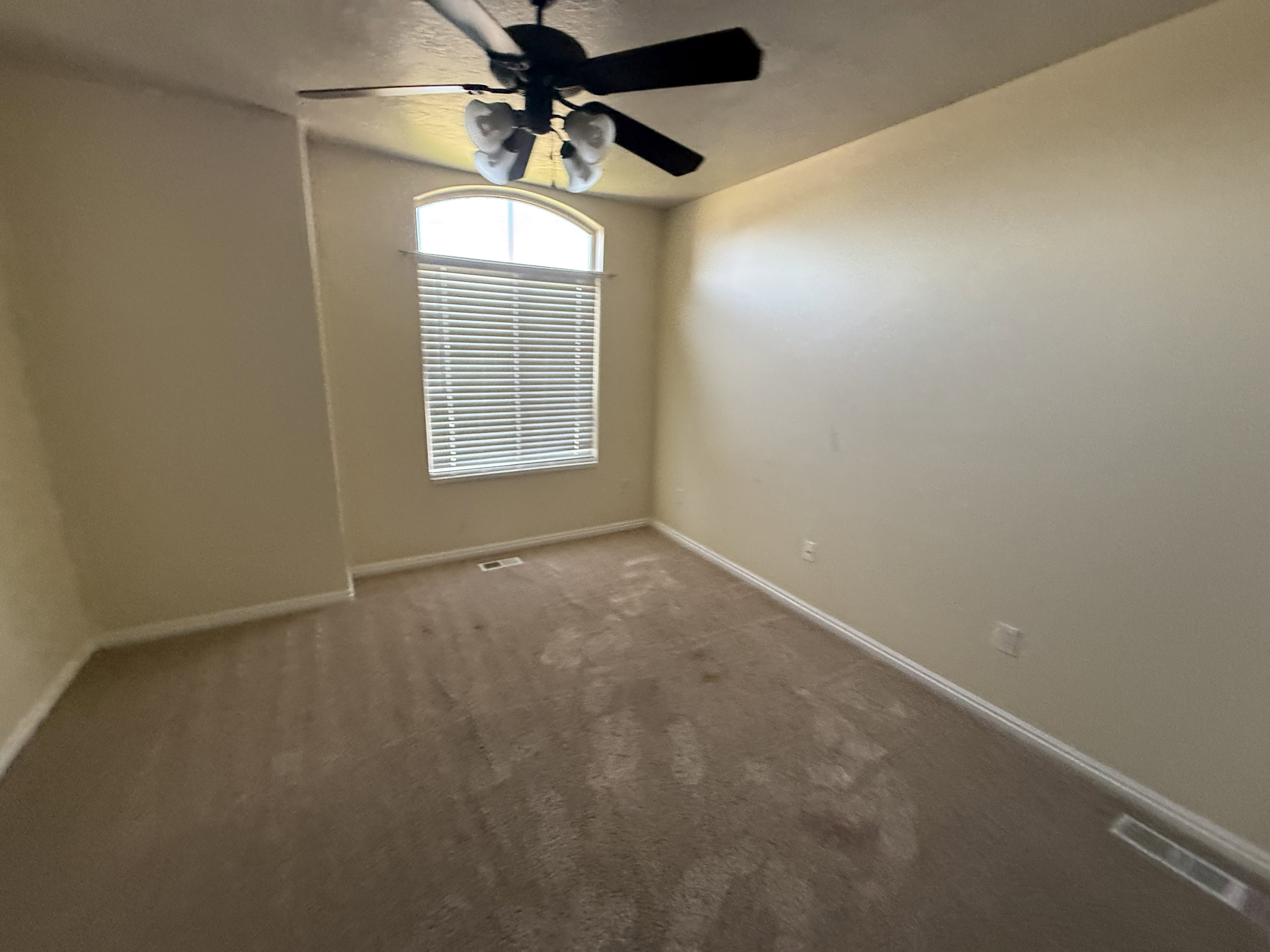 Room featuring a high arched window with horizontal blinds, neutral wall paint, and a ceiling fan with integrated lighting