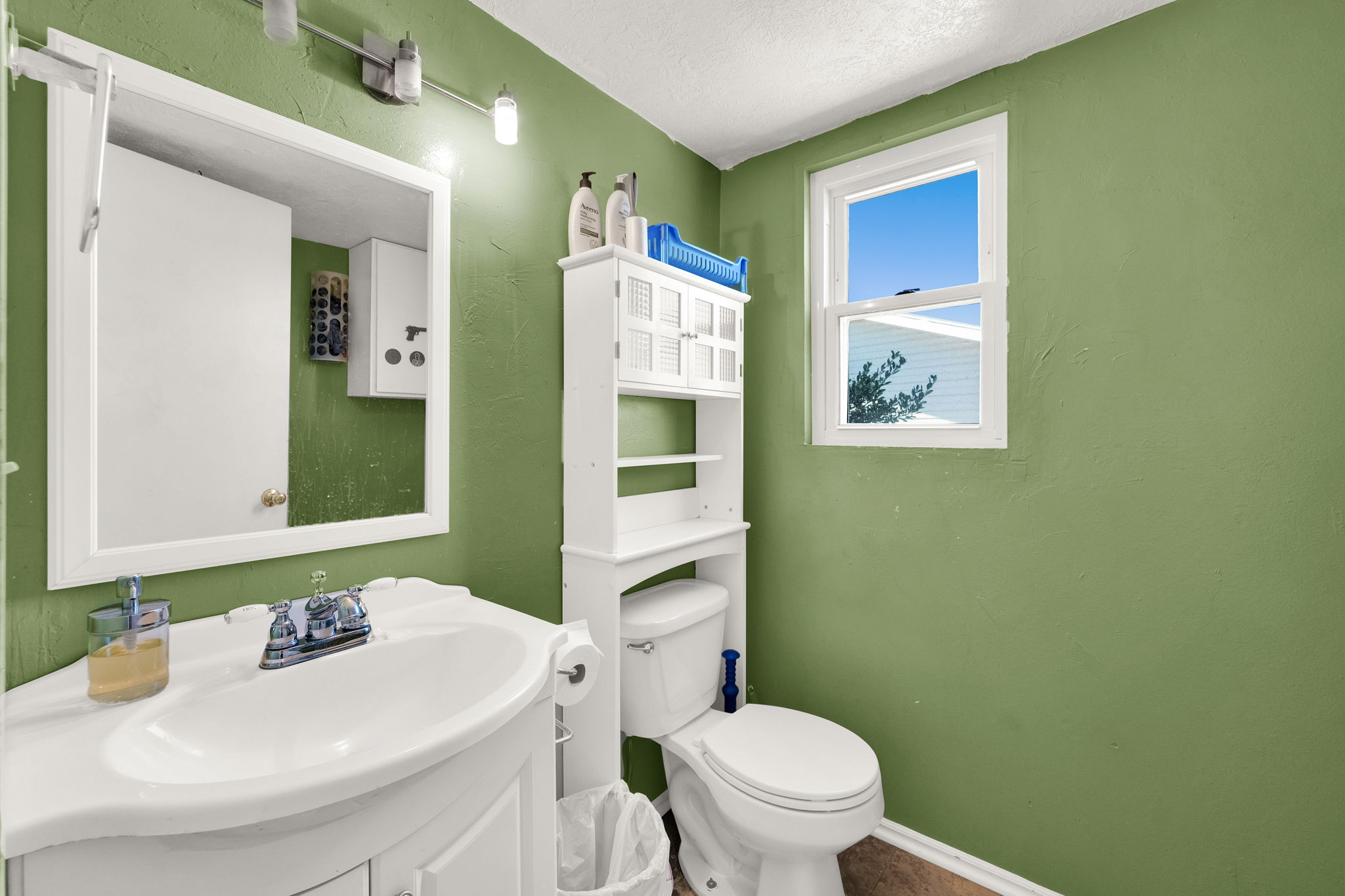 Bathroom featuring a single window, white vanity with integrated sink, chrome faucet, wall mirror, and toilet with an over-the-toilet storage unit
