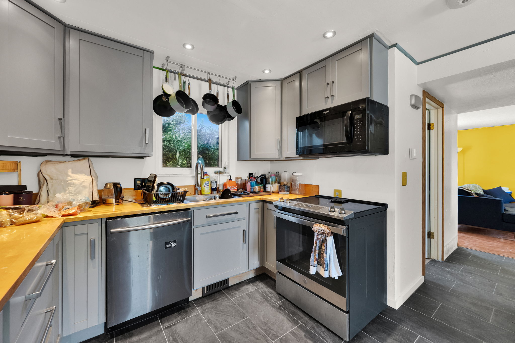 Kitchen featuring grey cabinetry, wood-finish countertops, stainless steel dishwasher, and a black over-the-range microwave