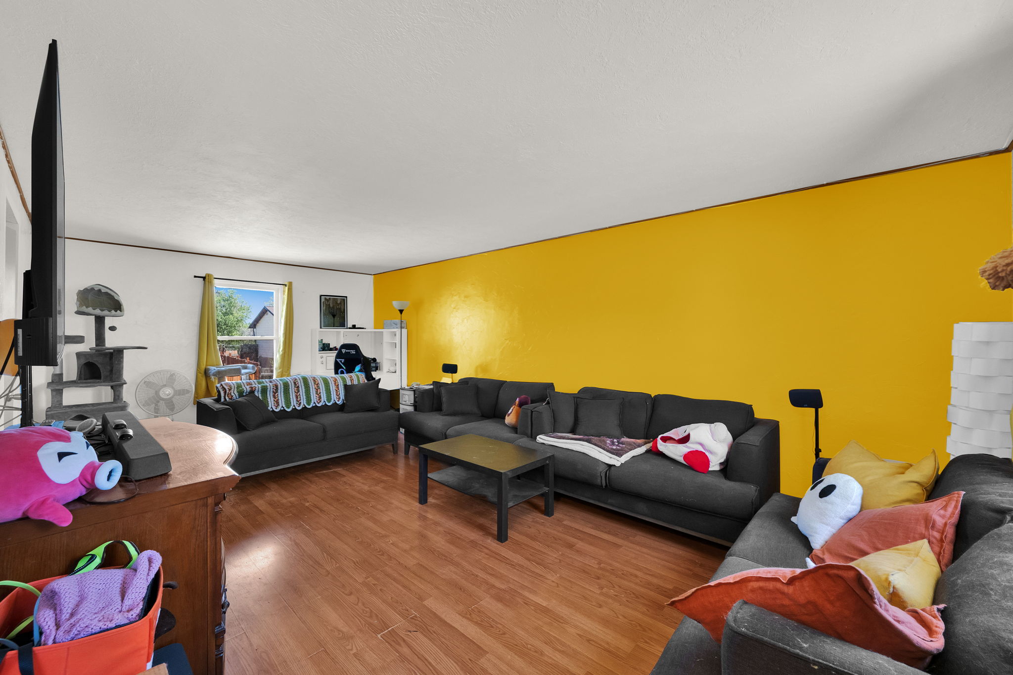 Spacious living area featuring wood-finish flooring, a prominent accent wall, and ample natural light from a large window