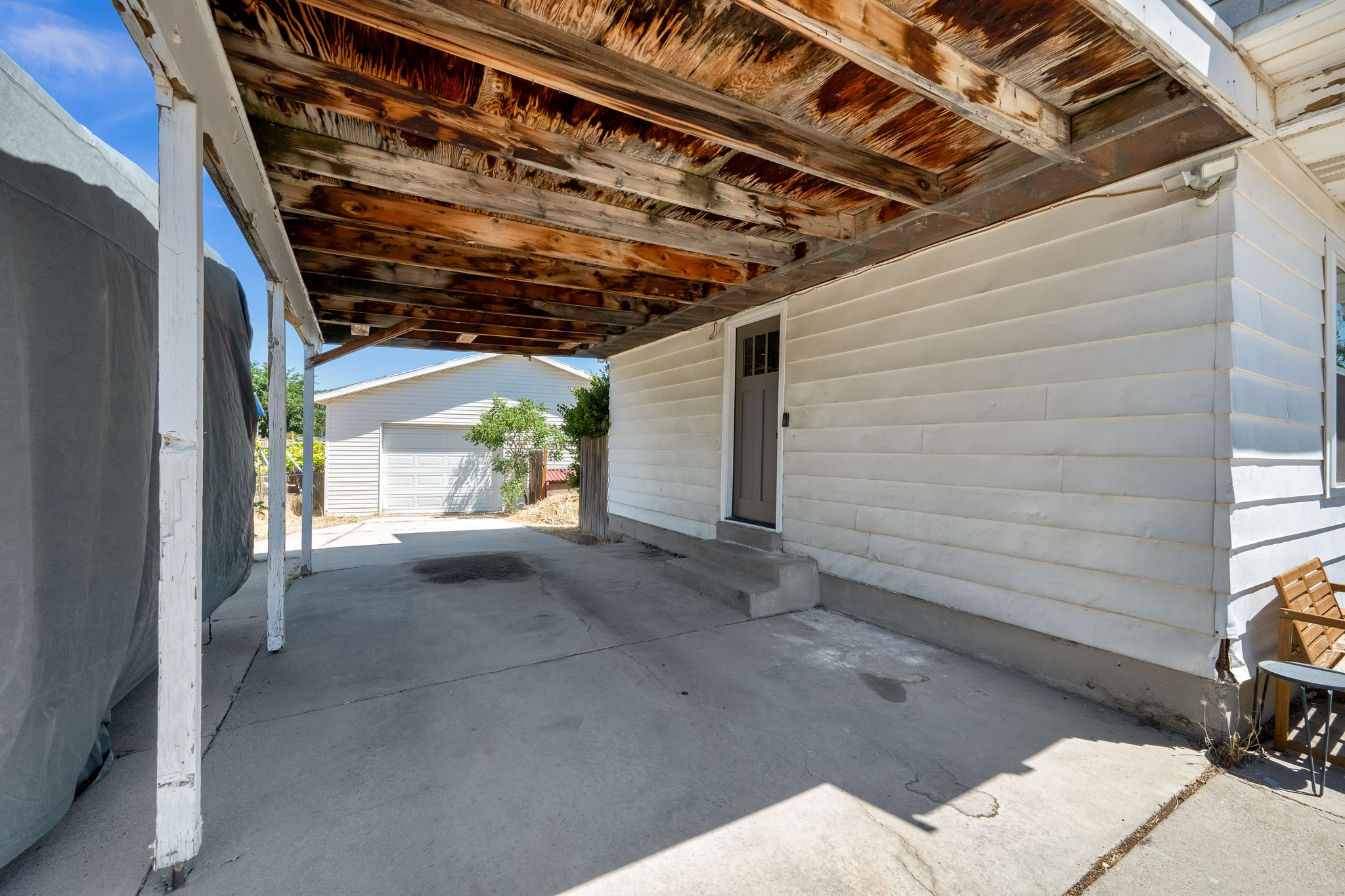 Carport with concrete slab, exposed wood ceiling, and white support posts