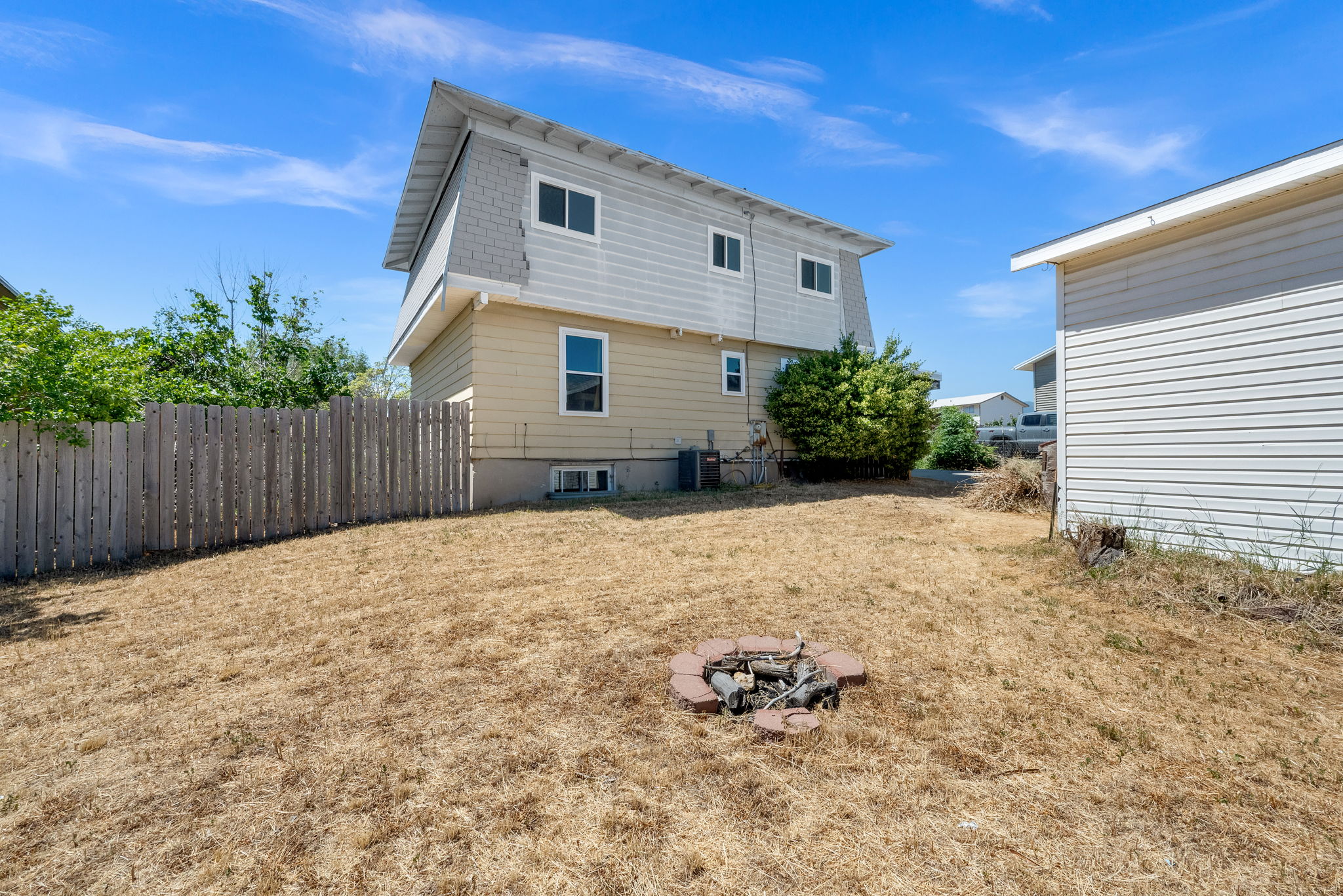 Fenced backyard with a stone-lined fire pit, featuring a two-story home with siding and a detached outbuilding