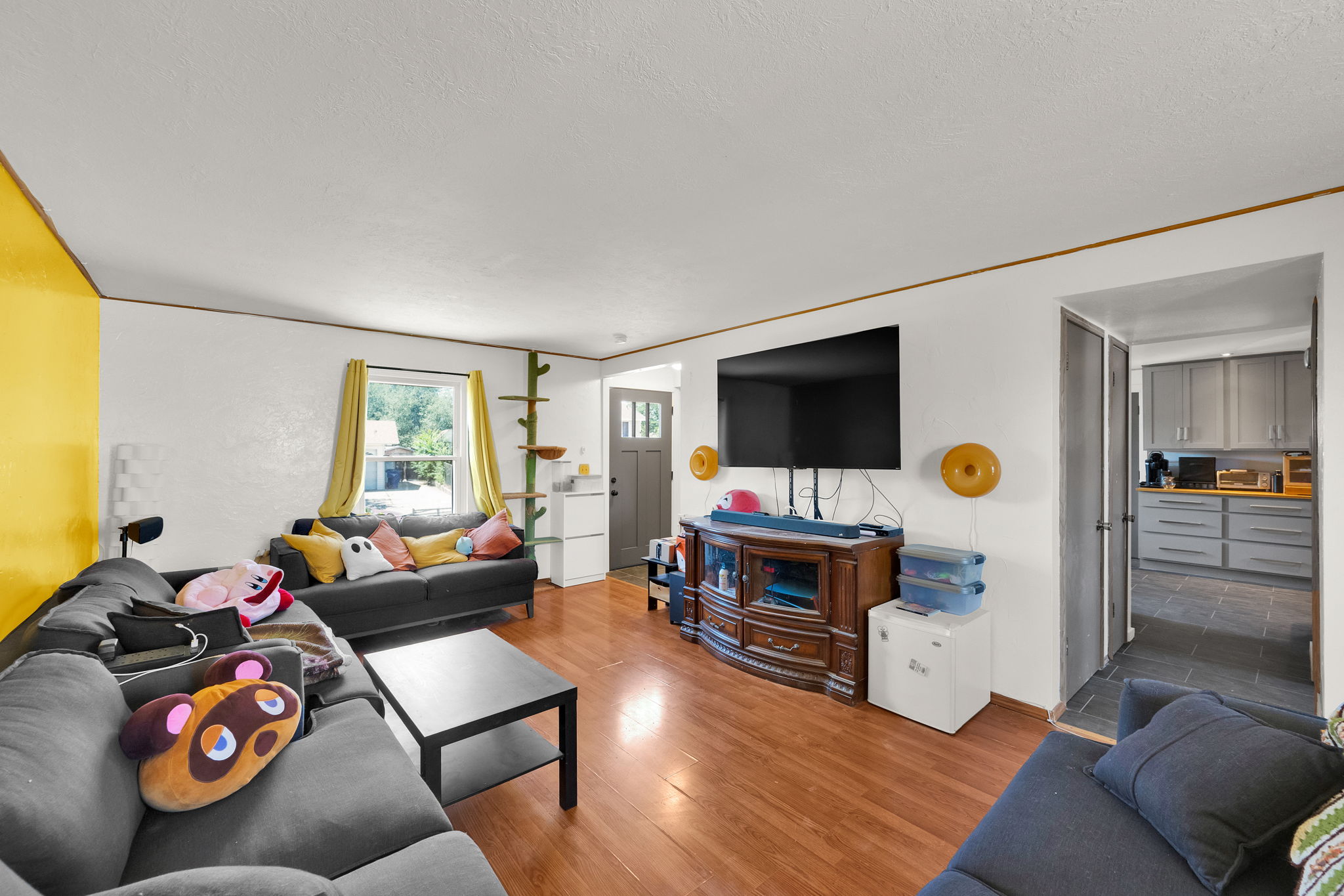 Living area featuring wood-finish flooring, white walls, and a large window with yellow drapes