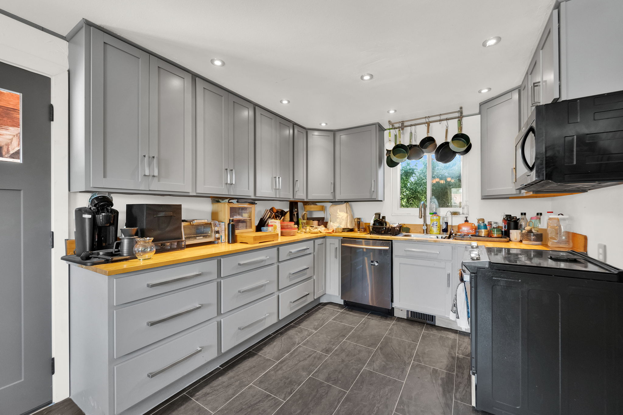 Kitchen featuring light grey cabinetry, wood-finish countertops, stainless steel dishwasher, black electric range, and dark tile flooring