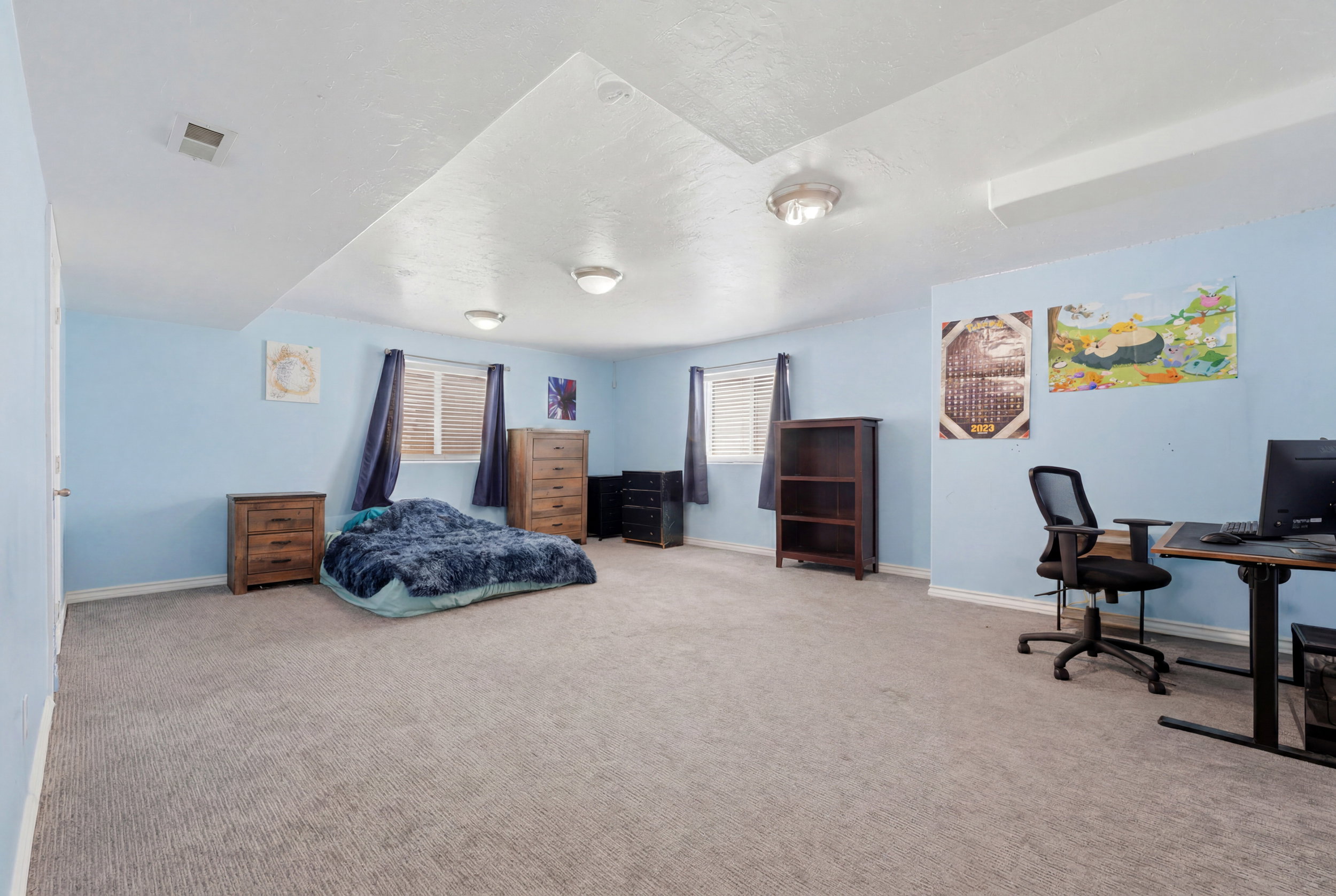Spacious room featuring light blue walls, gray carpeting, dual windows with blinds, and recessed ceiling lighting