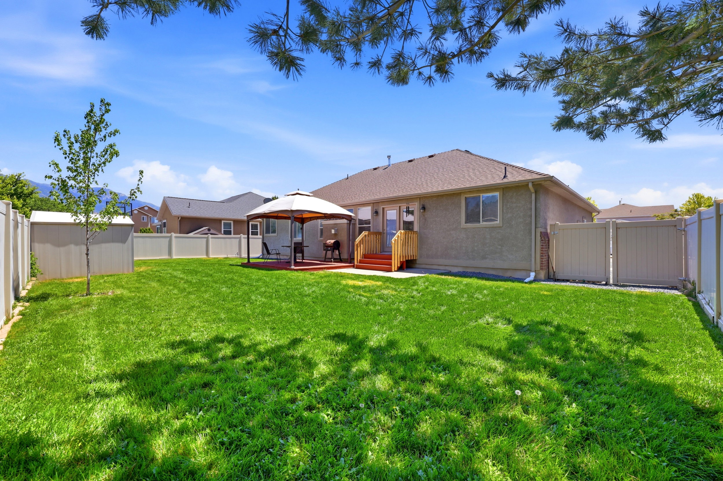 Expansive backyard featuring a large green lawn, covered patio area, storage shed, full privacy fencing, and a stucco exterior on the home