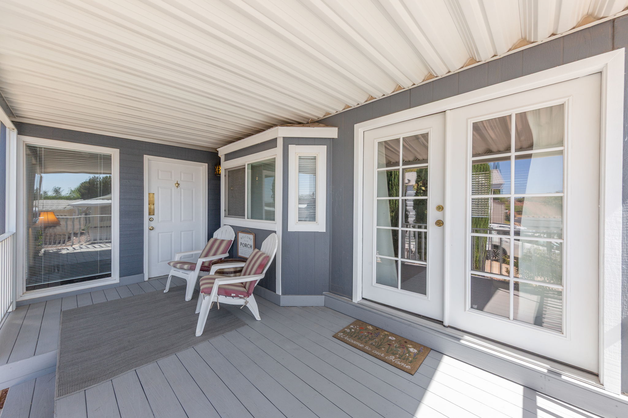 Covered porch featuring a gray wood-finish deck, white railing, and paneled siding