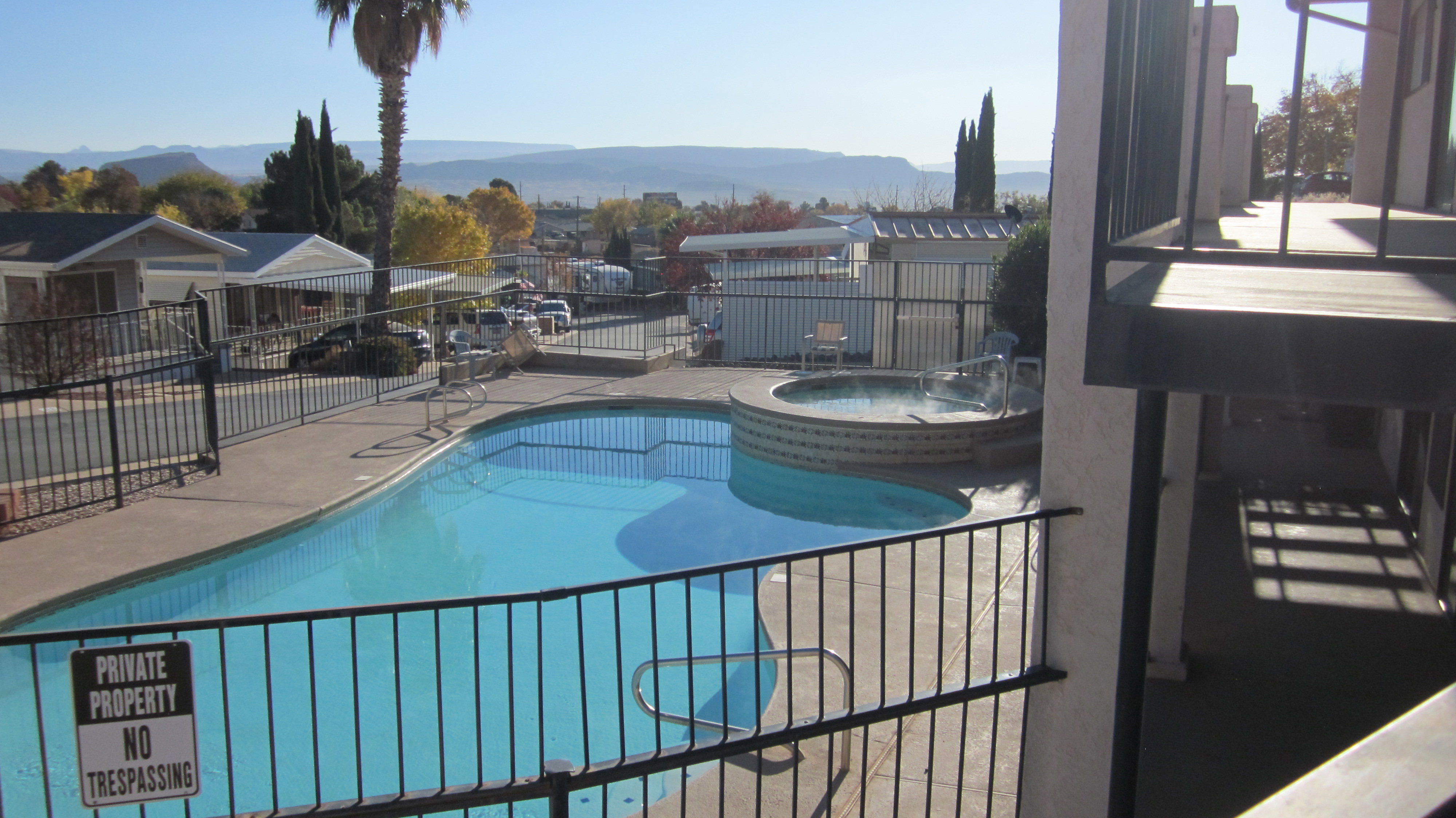 Outdoor swimming pool with integrated hot tub, surrounded by a black wrought iron fence