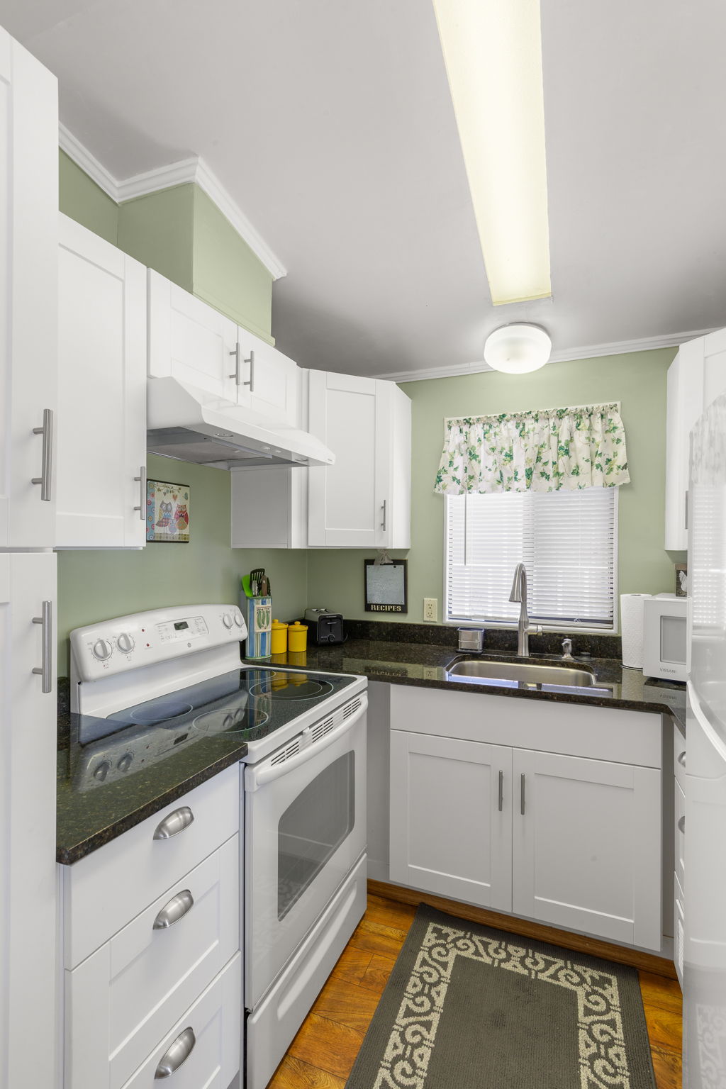 Kitchen featuring white shaker-style cabinetry, dark countertops, a stainless steel sink with a gooseneck faucet, a white electric range, and wood-finish flooring