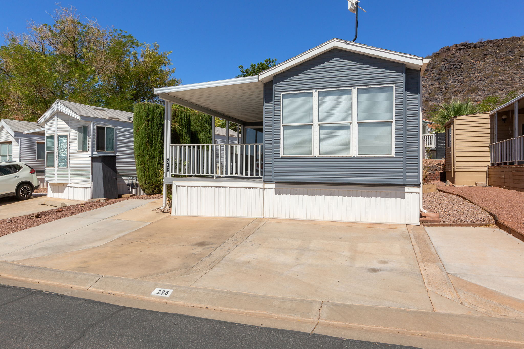 Exterior featuring gray horizontal siding, white trim, a covered porch, an asphalt driveway, and a concrete parking pad