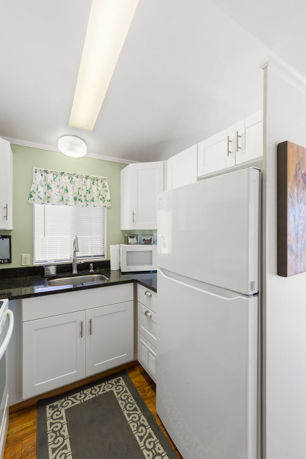 Kitchen featuring white cabinetry, dark countertops, a stainless steel sink with a gooseneck faucet, and wood-finish flooring