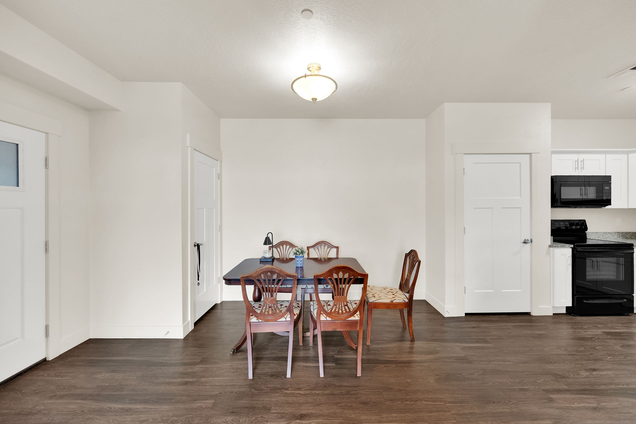 Open-concept dining area with wood-finish flooring, white walls, and a semi-flush ceiling light fixture