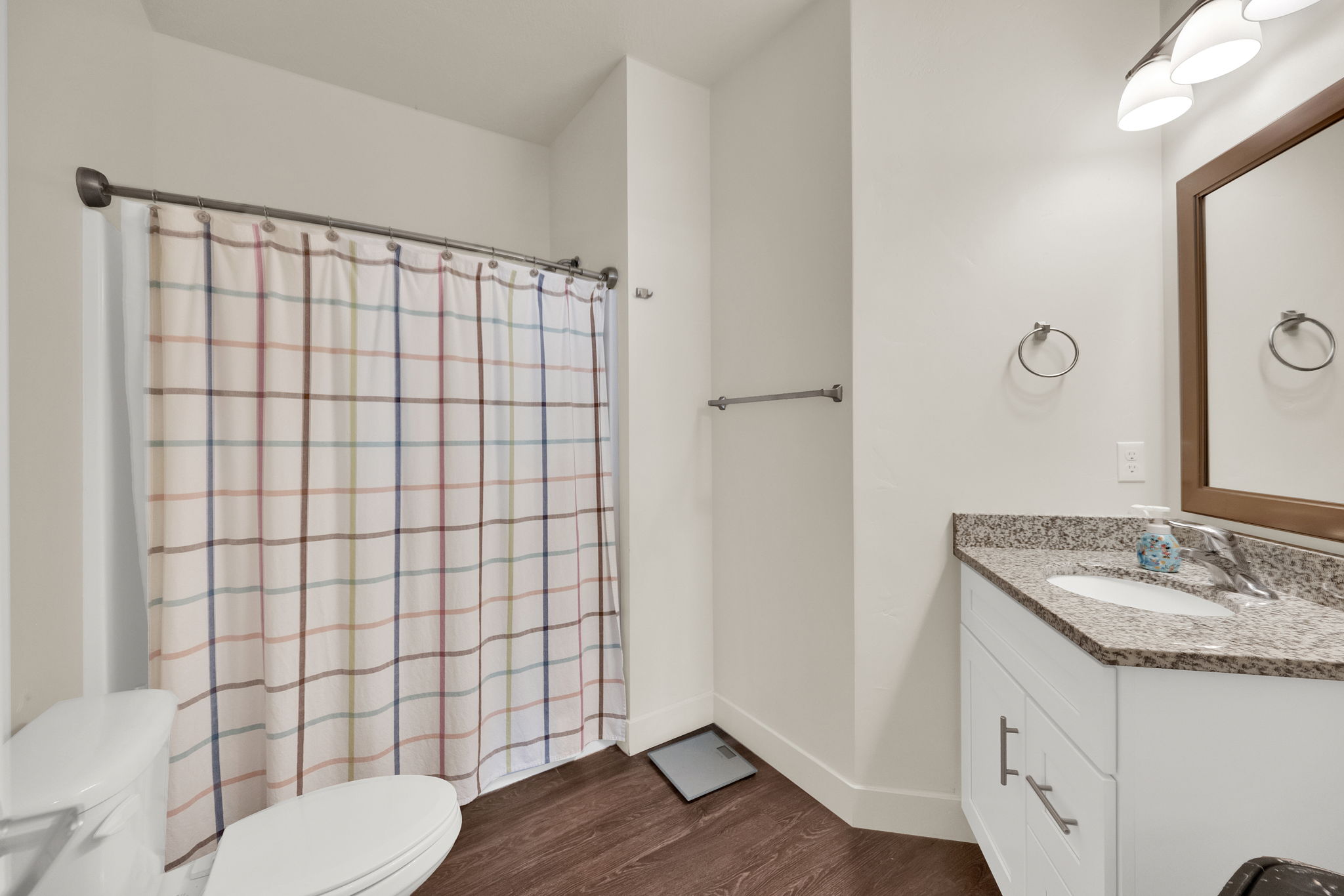 Bathroom featuring a white vanity with a speckled countertop, a rectangular mirror, and wood-finish flooring