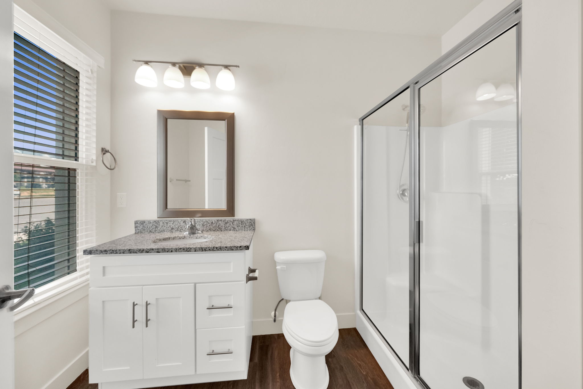 Bathroom featuring a single white vanity with a speckled countertop, a framed mirror, and a wall-mounted light fixture