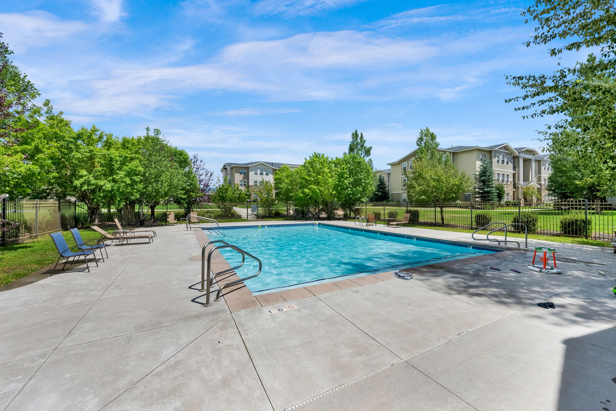 Rectangular outdoor swimming pool featuring concrete decking, metal handrails, and a black wrought iron fence